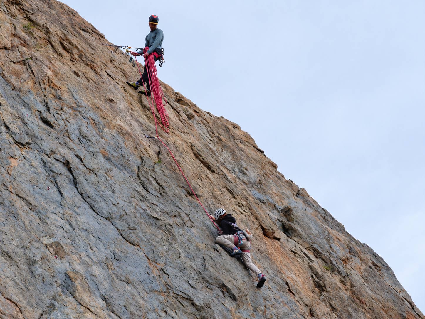 Evan belaying from the top of a crag as a climber works up the rock face below.