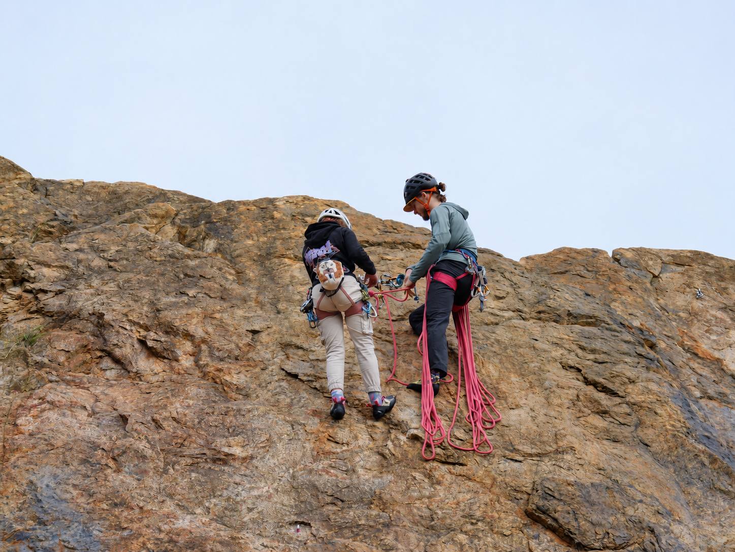 Evan and a climber at the top of a sunlit rock face, a pink rope coiled at their feet.