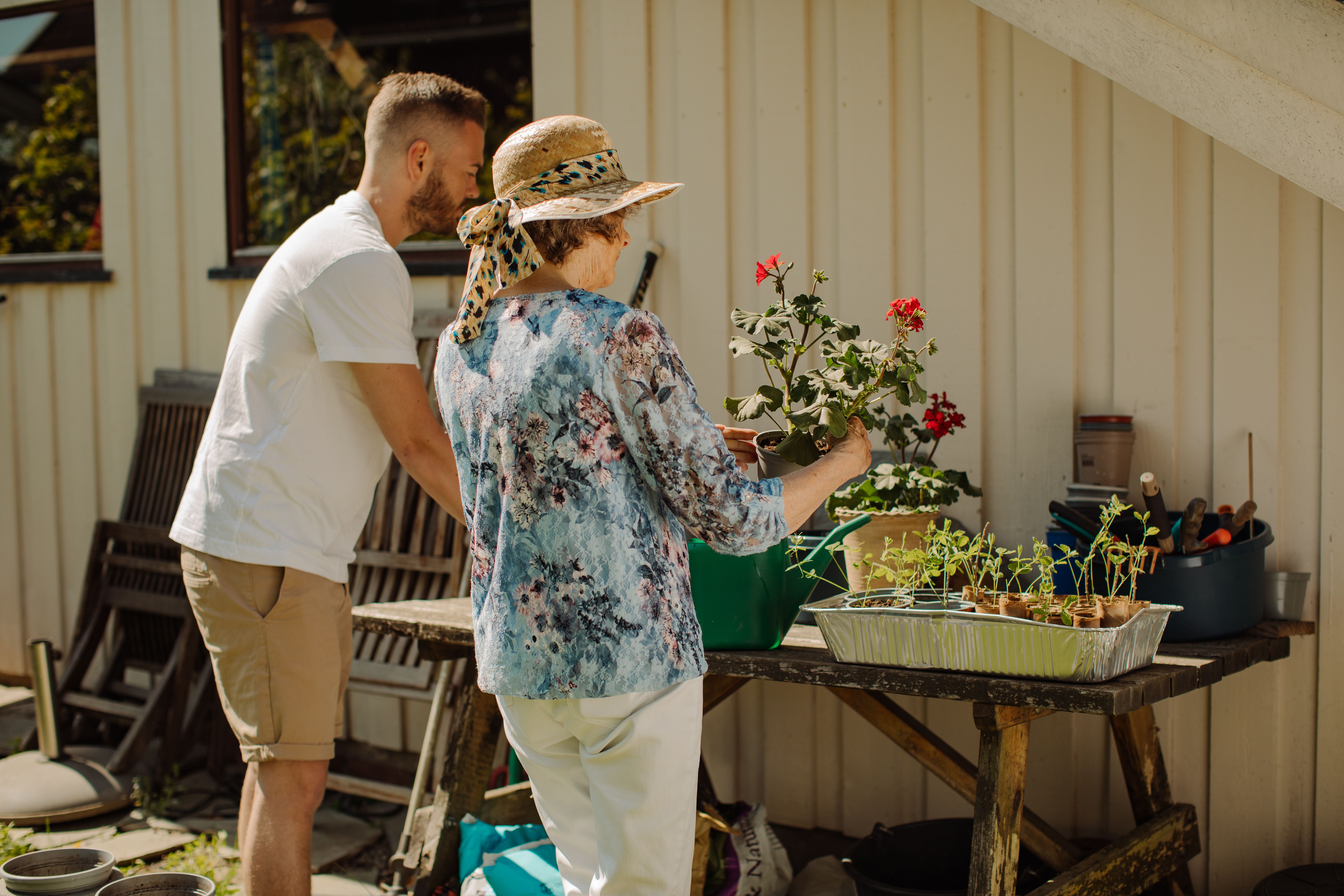 En ung mann og en eldre dame står ute og potter om planter og blomster