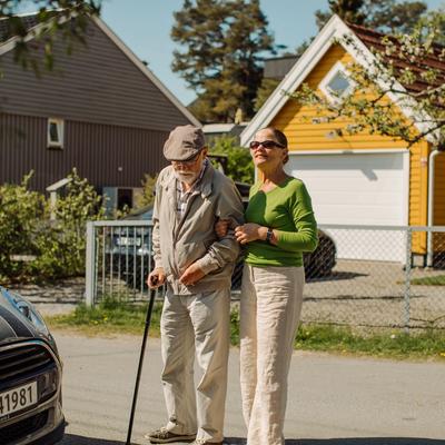 En dame leier en eldre herre med stokk
