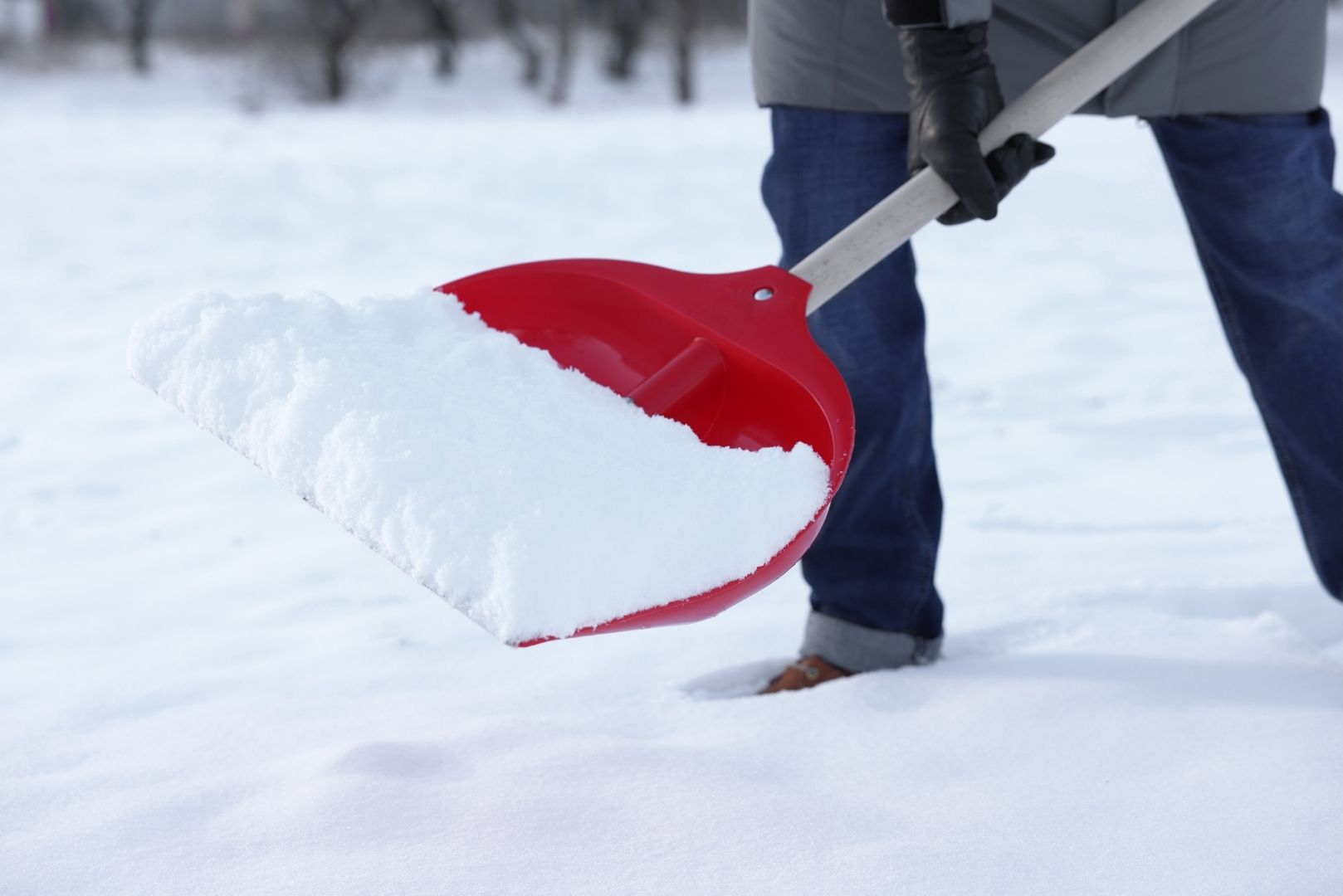 En person måker snø med en rød spade