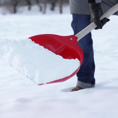 En person måker snø med en rød spade