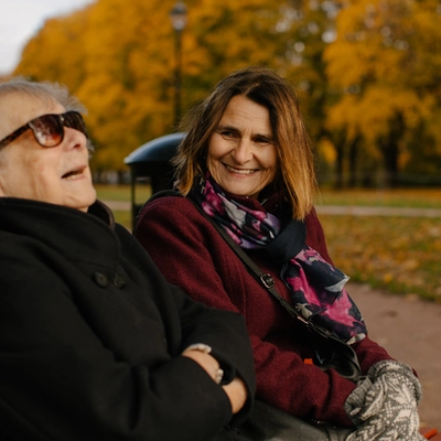 To damer sitter ute på en benk og ler