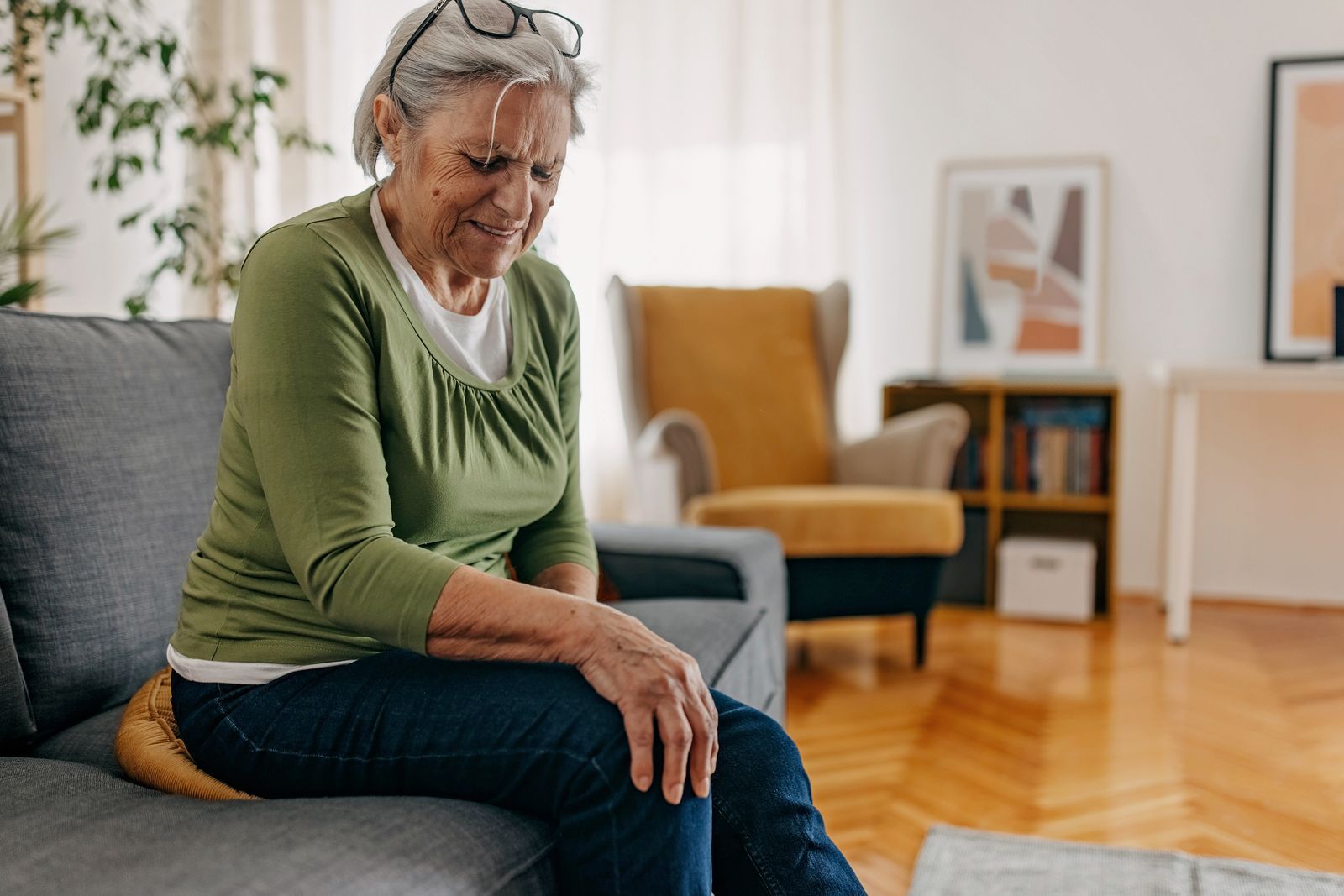 En eldre dame sitter på sofaen og holder seg til et smertefullt kne