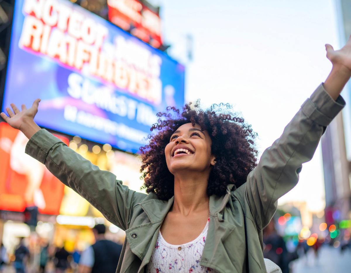 a woman standing in front of a billboard, she is excited and throwing her arms out