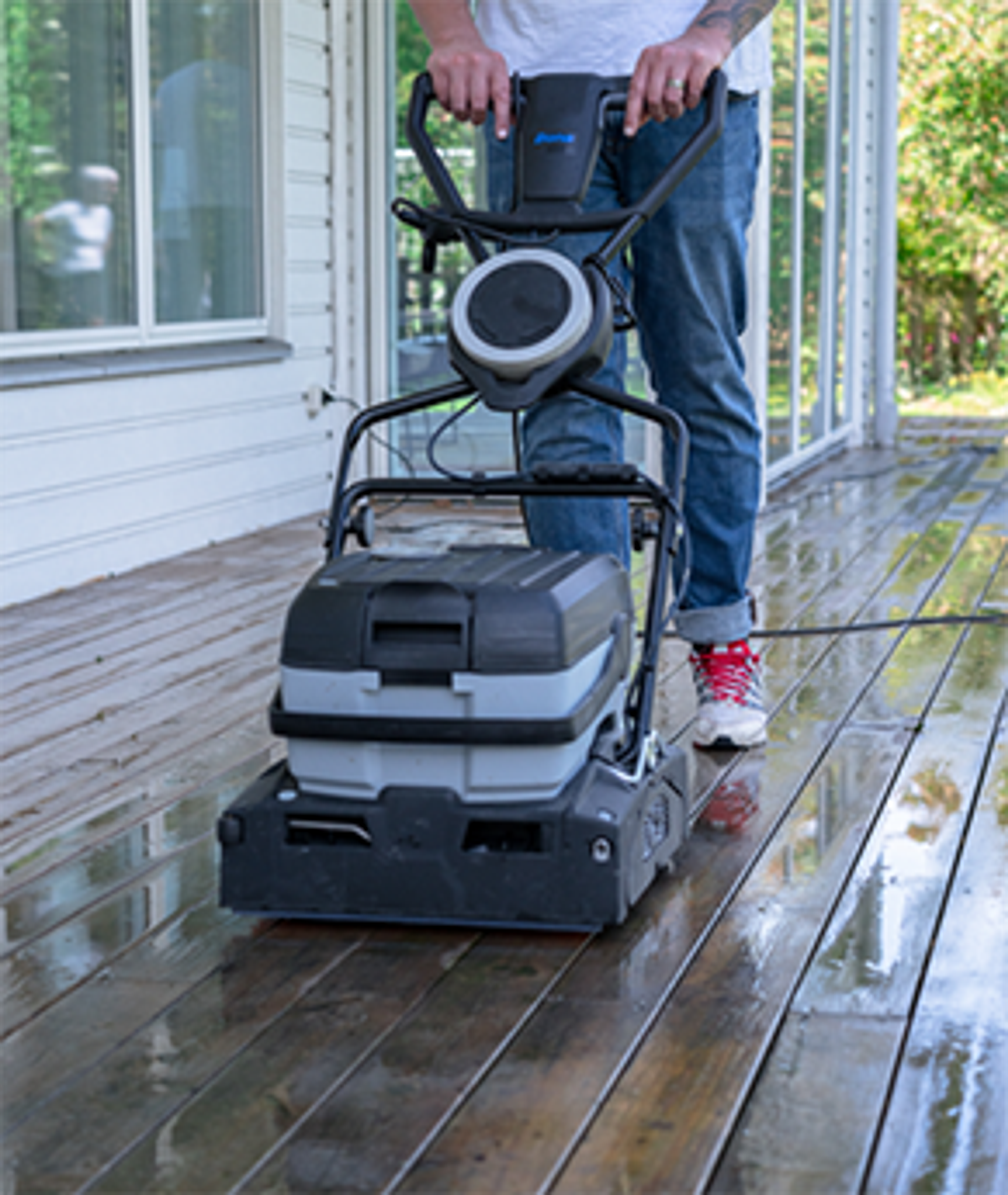 Person cleaning a wet wooden deck with a floor scrubber.