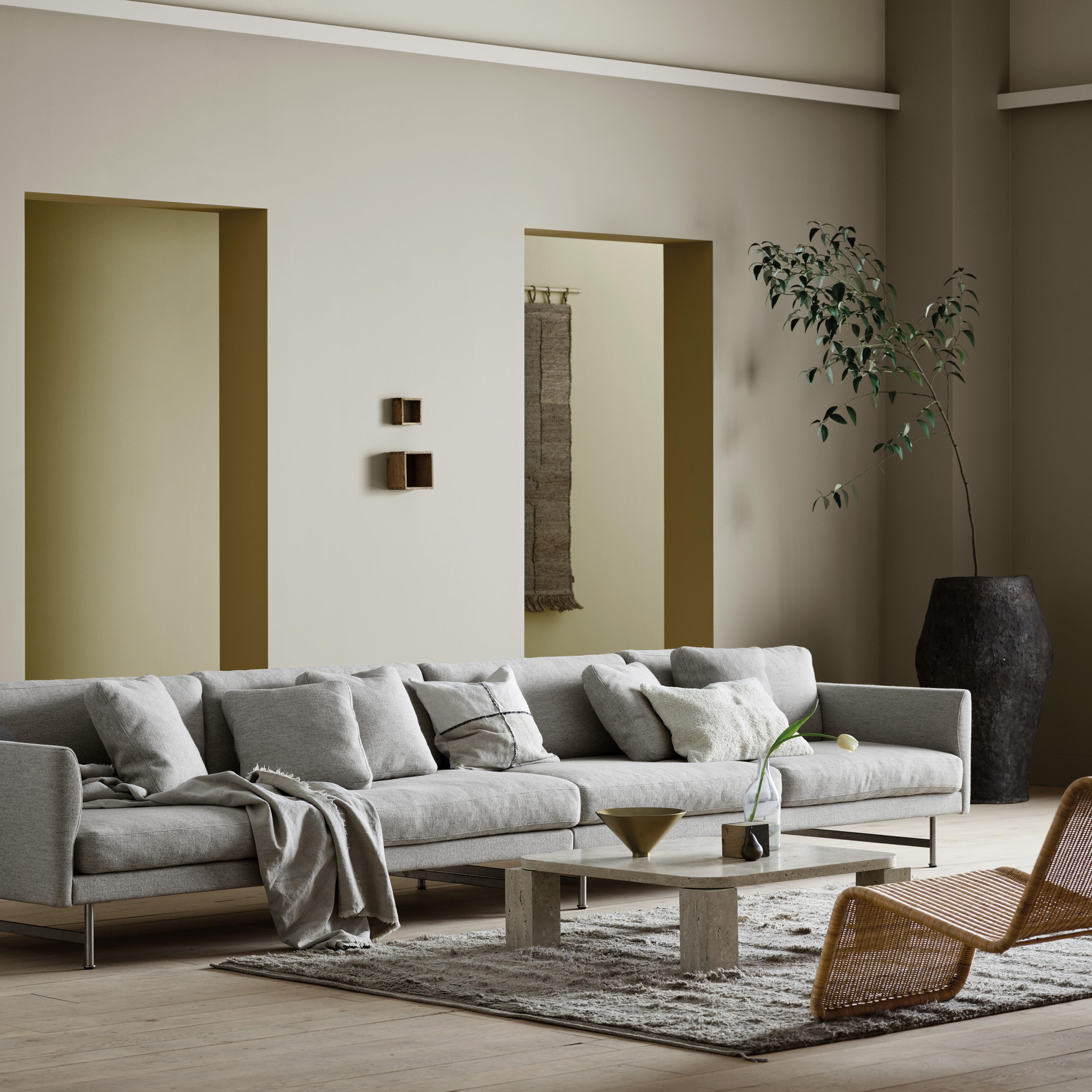 A minimalist living room with a long gray sofa, stone coffee table, and large potted plant.