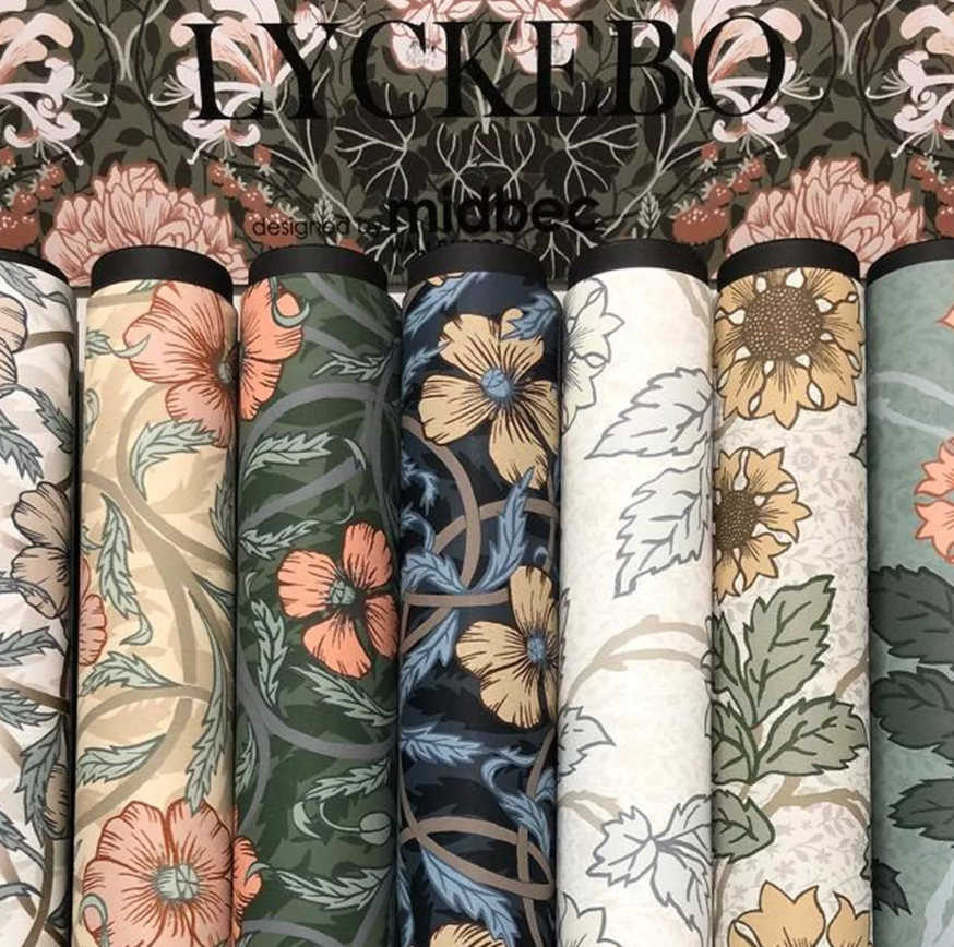 Display of multiple wallpaper rolls with diverse floral patterns and colors, text "LYCKEBO designed by midbec" above.