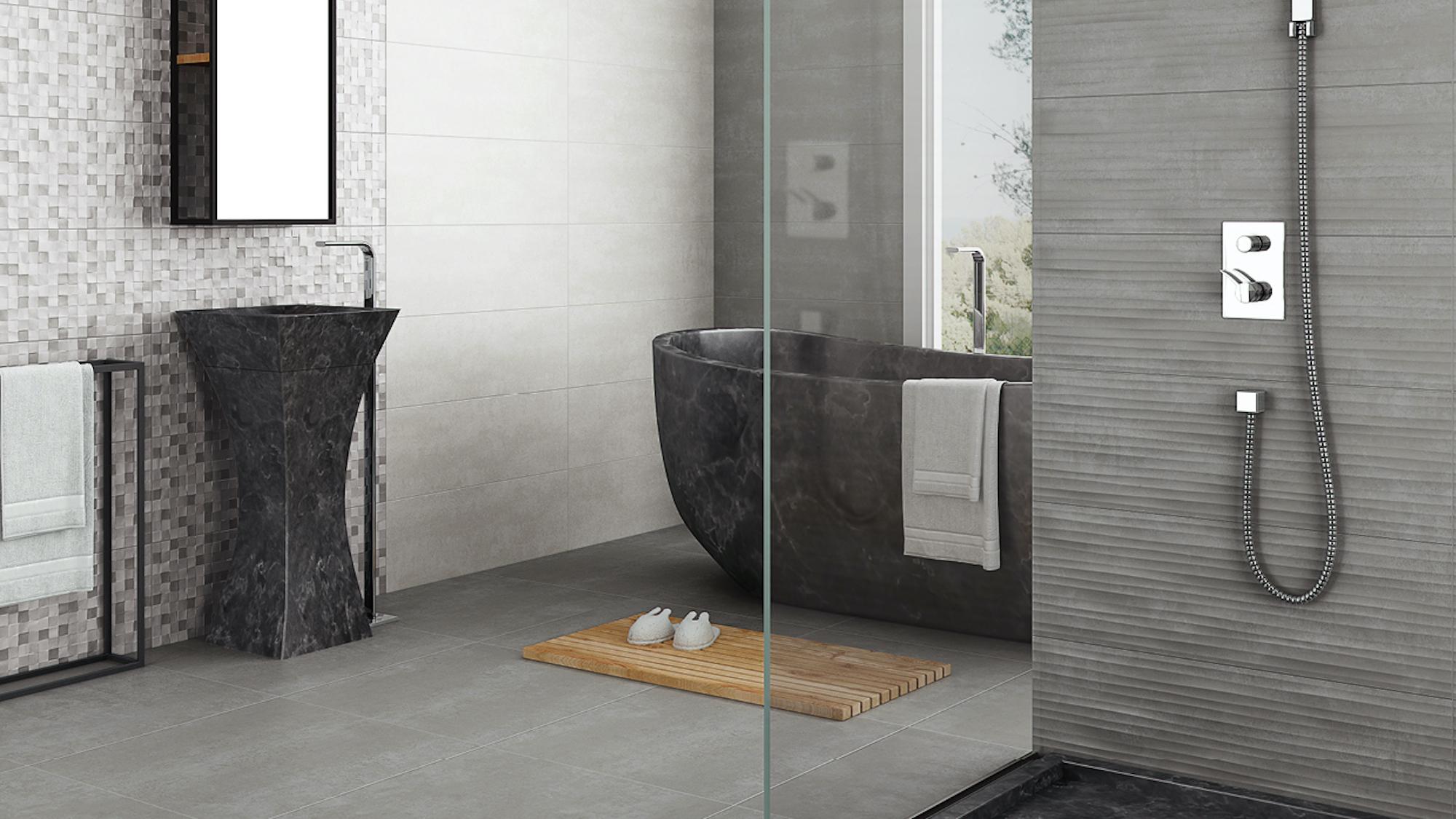 A modern bathroom with a dark stone pedestal sink, freestanding tub, and a shower with grey tiled walls.