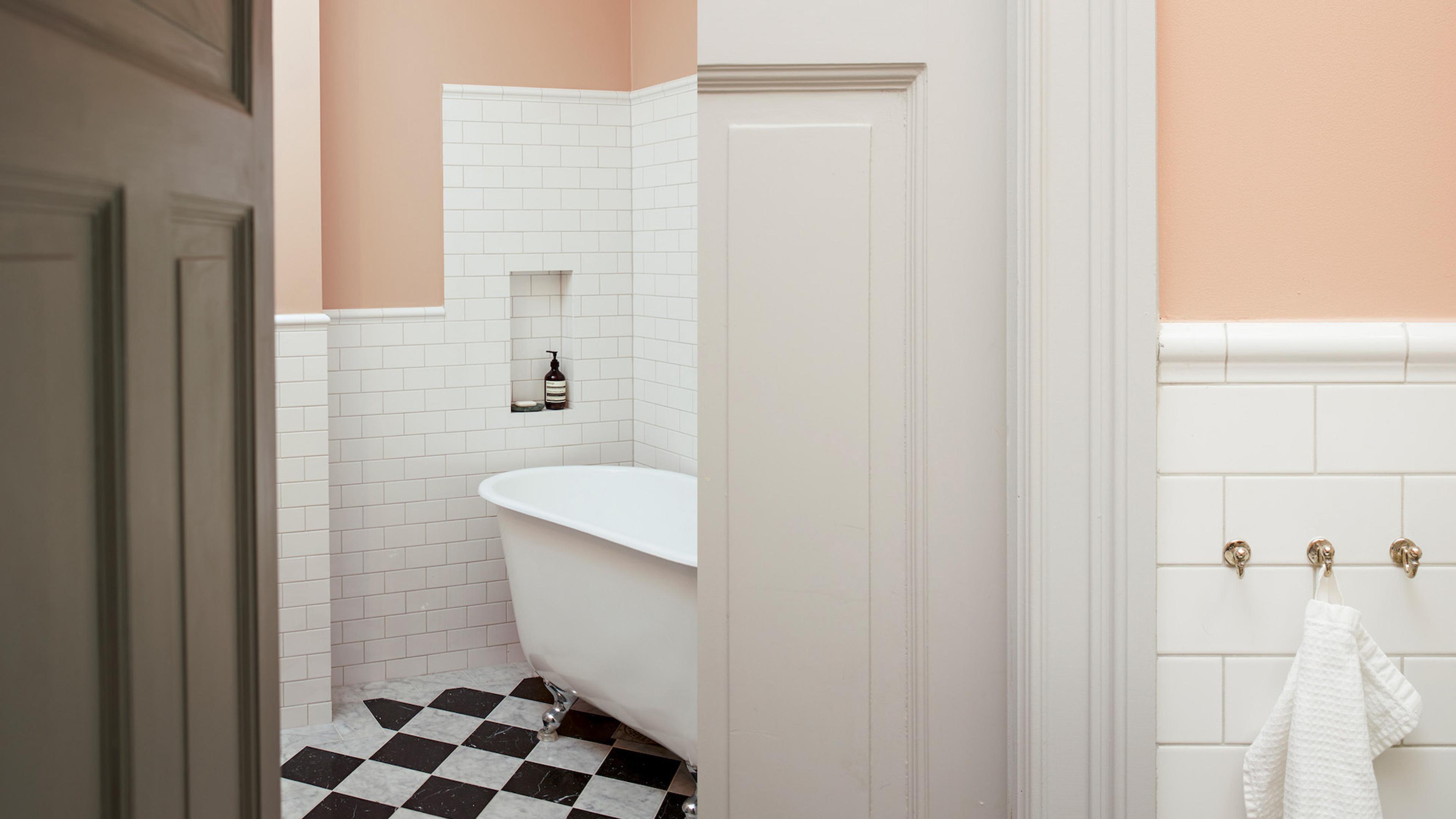 A bathroom featuring a white clawfoot tub on a black and white checkered floor, with white subway tile wainscoting and peach walls.