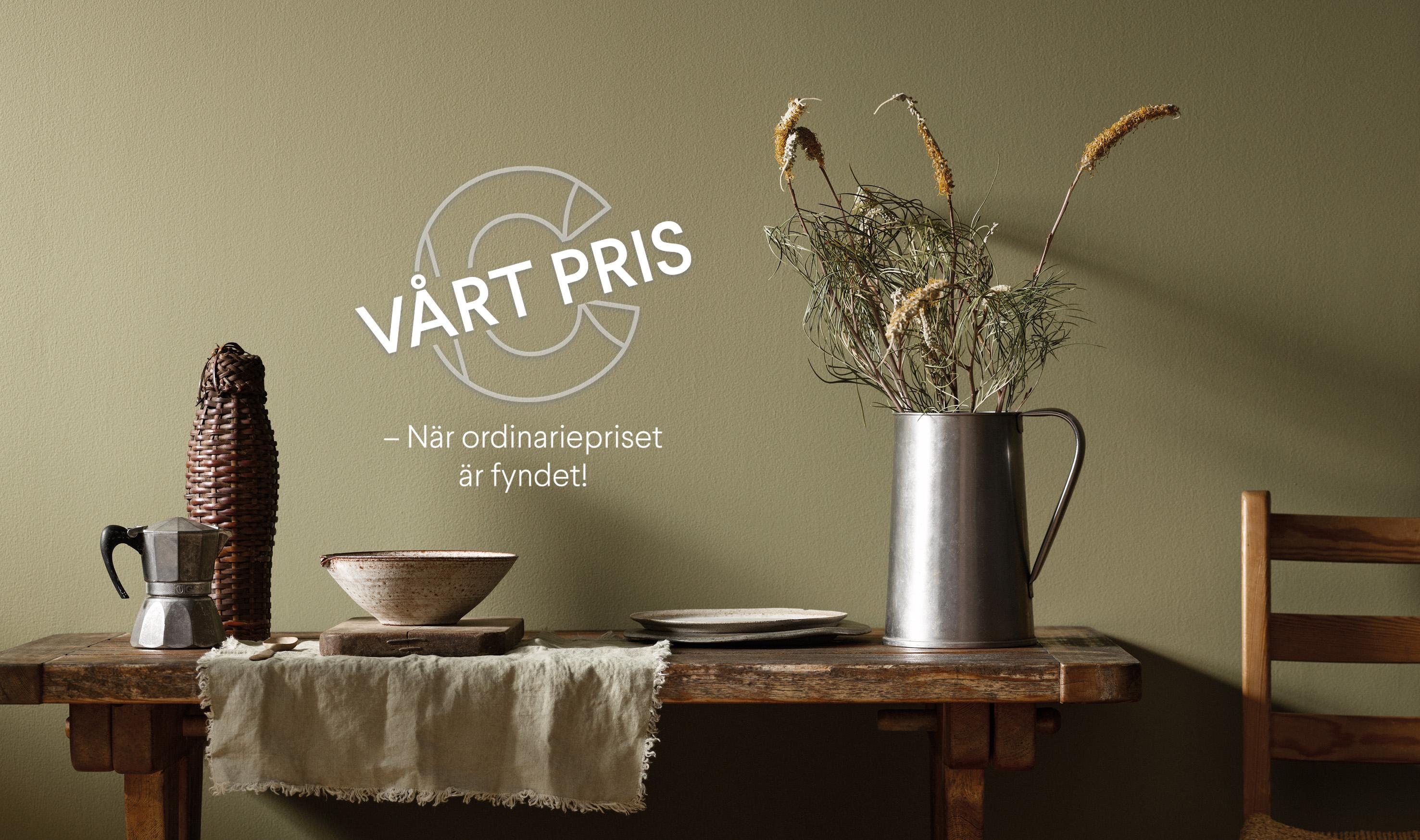 A rustic table with a moka pot, ceramic bowl, and dried plants in a pitcher against an olive green wall. White text reads: "VÅRT PRIS – När ordinariepriset är fyndet!".