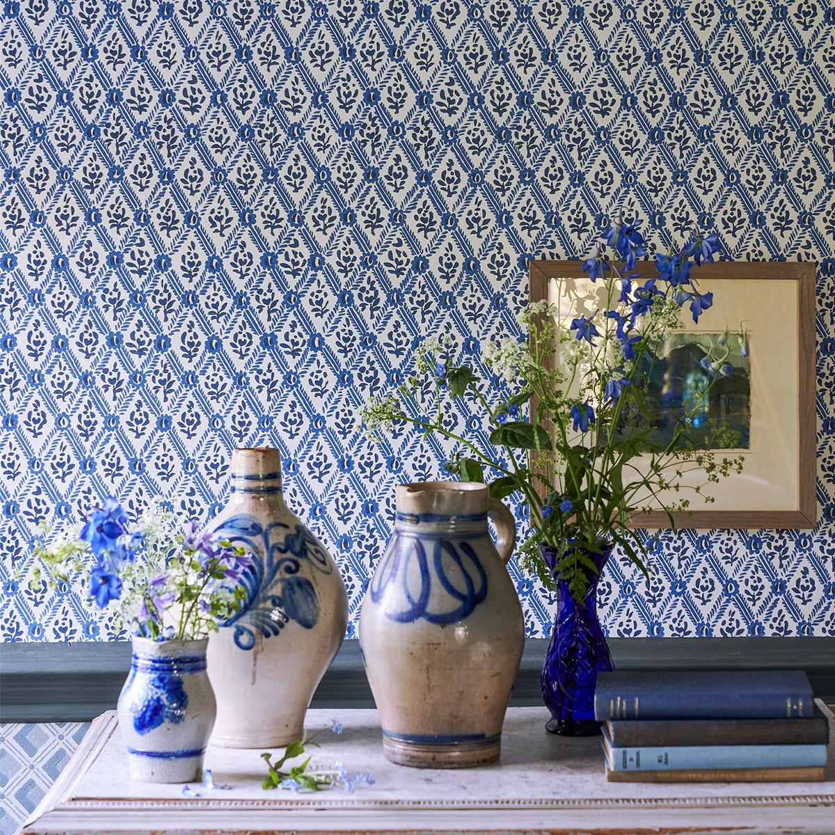 Blue and white room decor featuring rustic pottery, blue flowers, and books against patterned wallpaper.