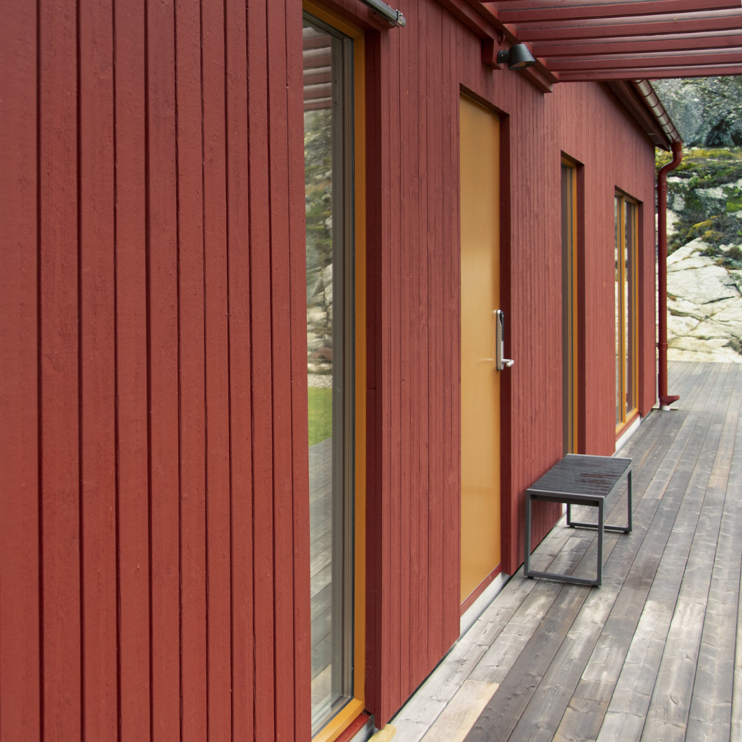 A red wooden building with a yellow door and large windows, next to a wooden deck.