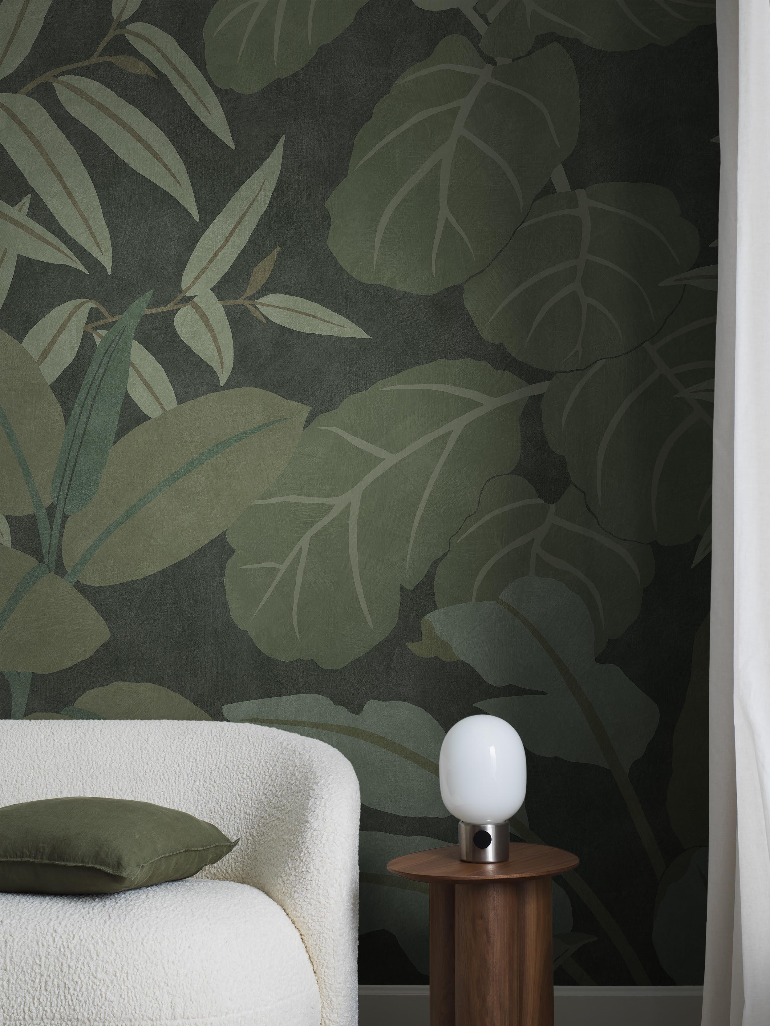 Dark green tropical leaf wallpaper behind a white textured sofa with a green pillow and a wooden side table holding a white globe lamp.