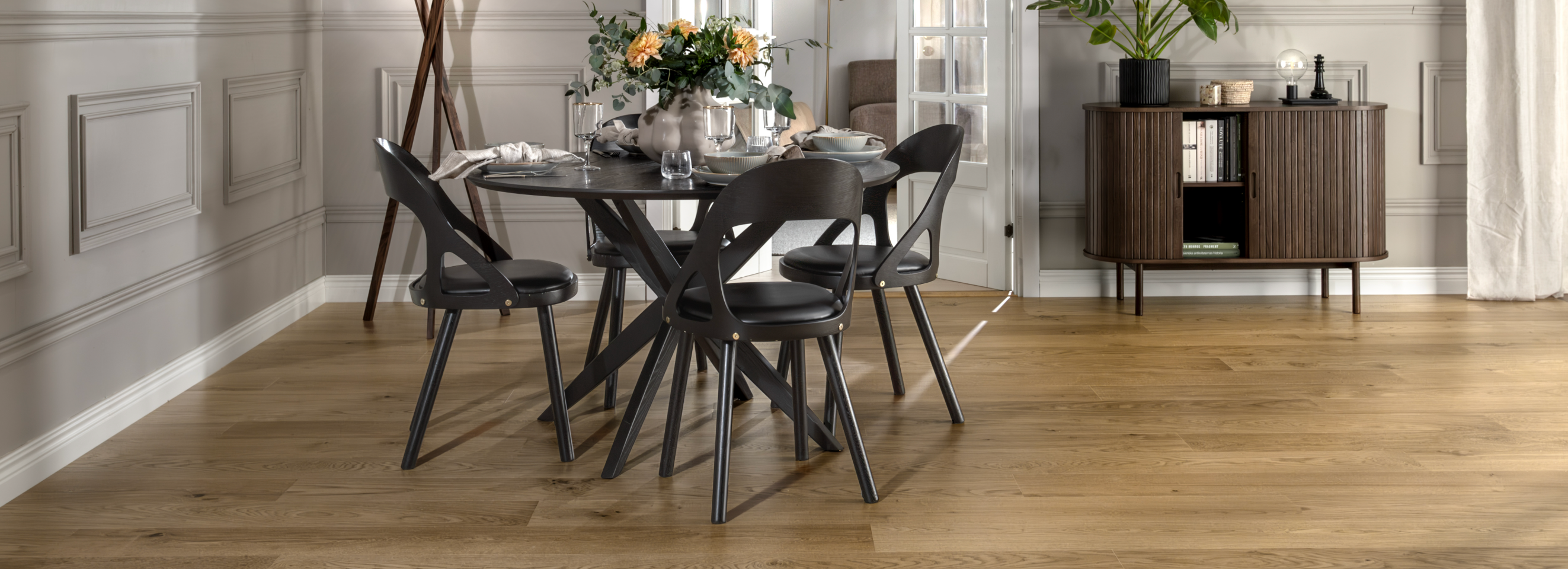 A modern dining room with light wood floors, a dark round table and chairs, and a brown cabinet.