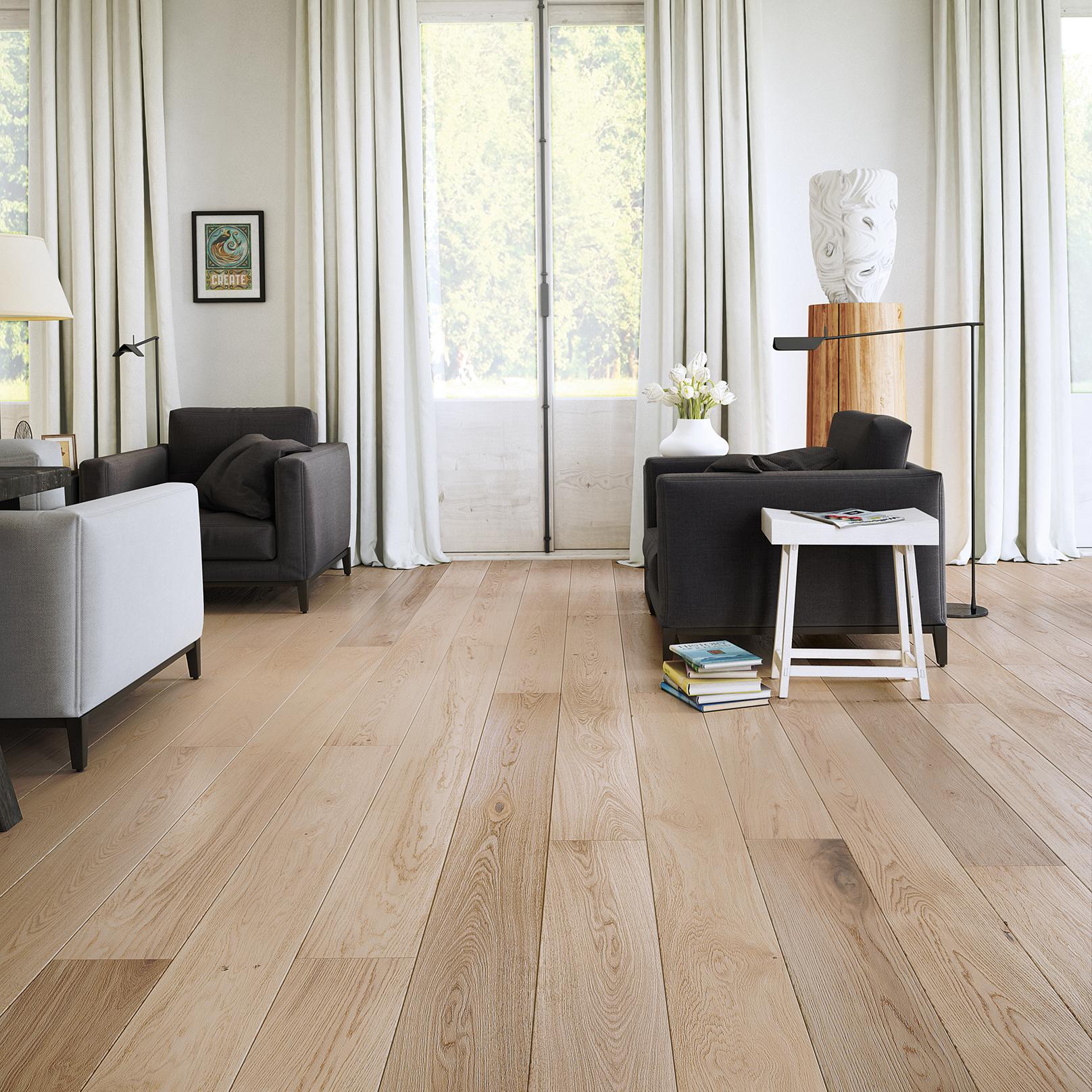 A bright living room with light wood floors, grey armchairs, and large windows with white curtains.