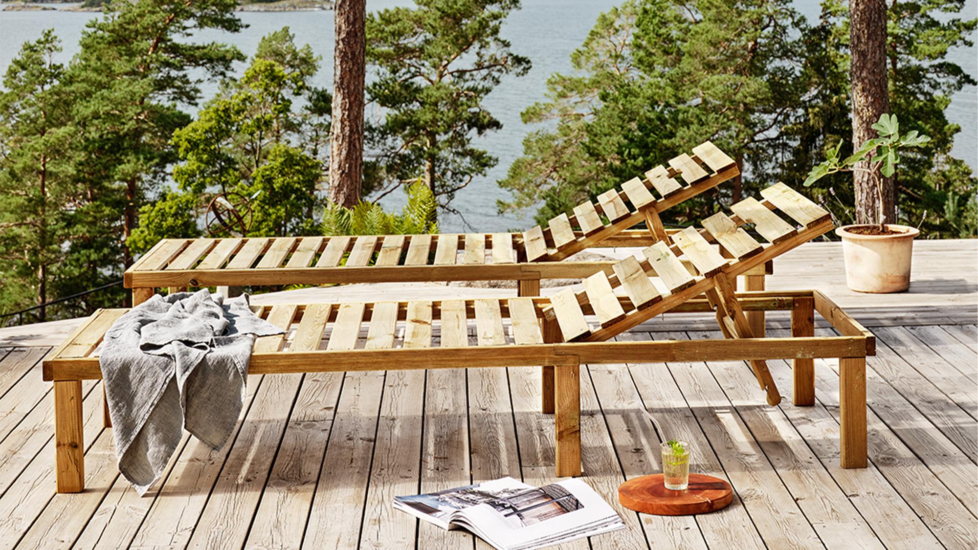 Two wooden sun loungers on a deck overlooking a forest and water.