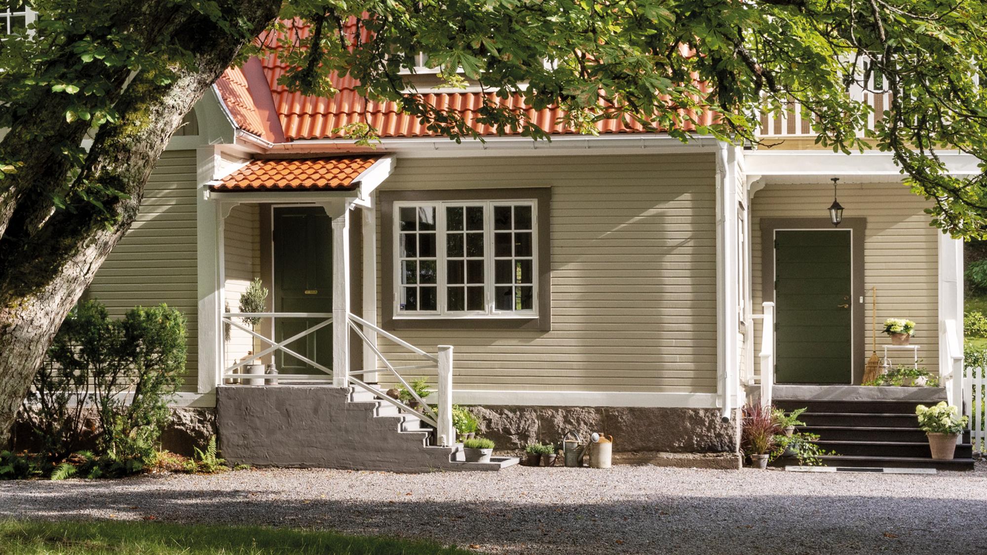 A light green house with a red tiled roof, two dark green doors, and white porches.