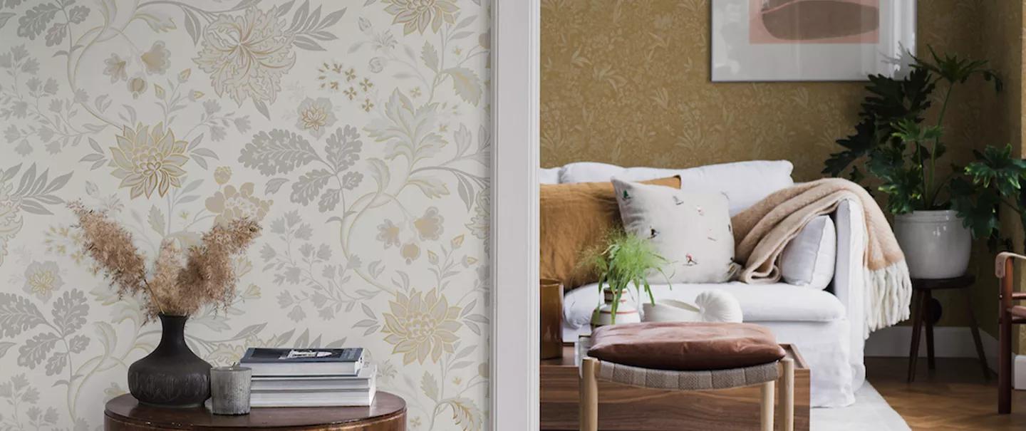 Two rooms separated by a doorway: the left features light floral wallpaper and a side table, the right a white sofa and gold textured wallpaper.