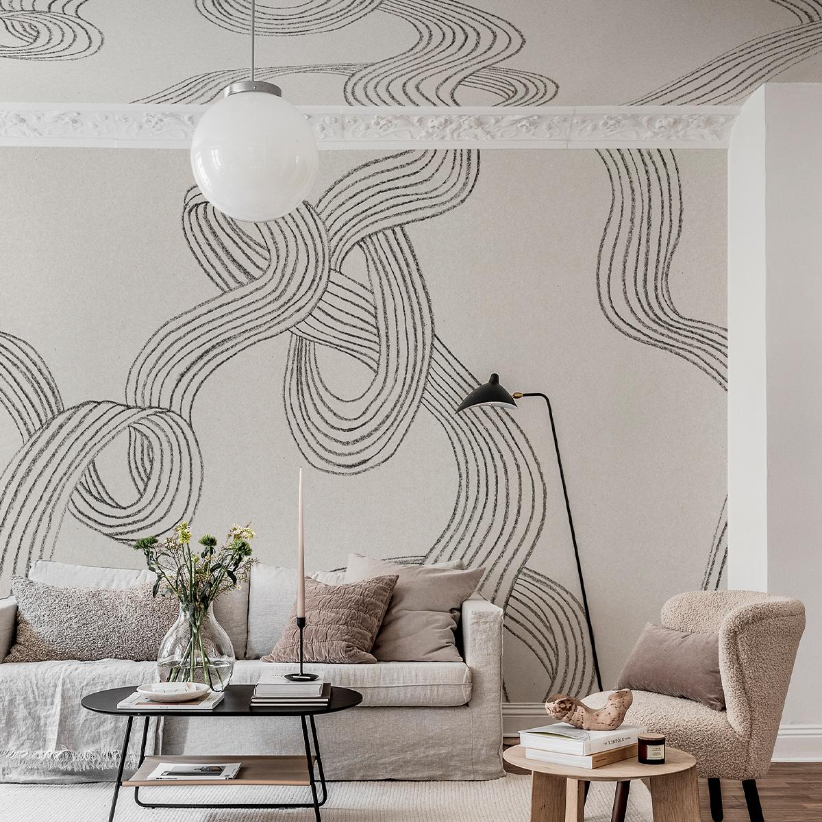 A living room featuring light wallpaper with intertwined black wavy lines, a light gray sofa, and a beige armchair.