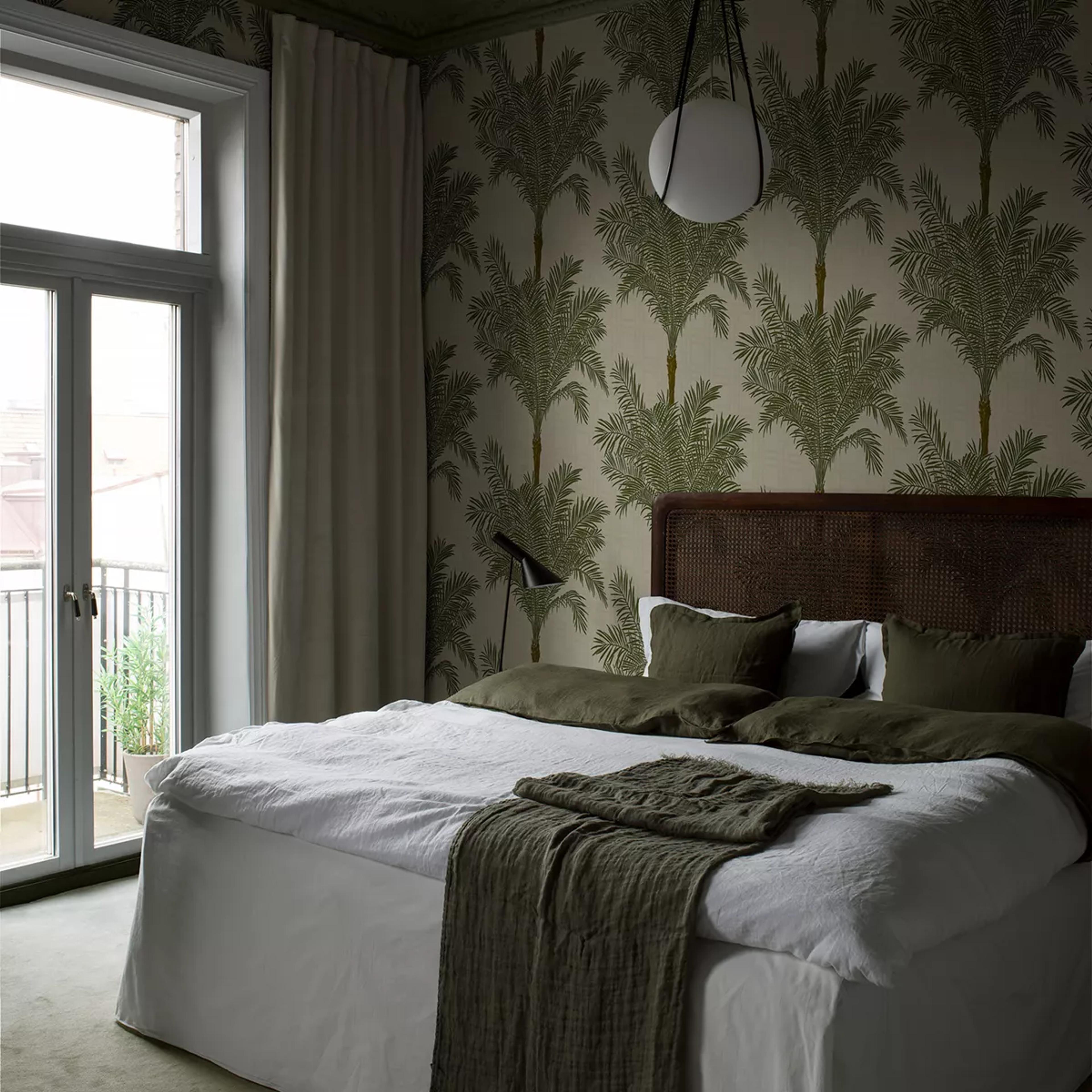 Bedroom with green palm tree wallpaper, a rattan headboard, a bed with white and olive green bedding, and a balcony door.