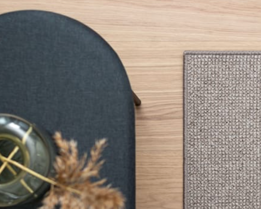Overhead view of a dark gray ottoman with dried pampas grass, light wood floor, and a gray textured rug.
