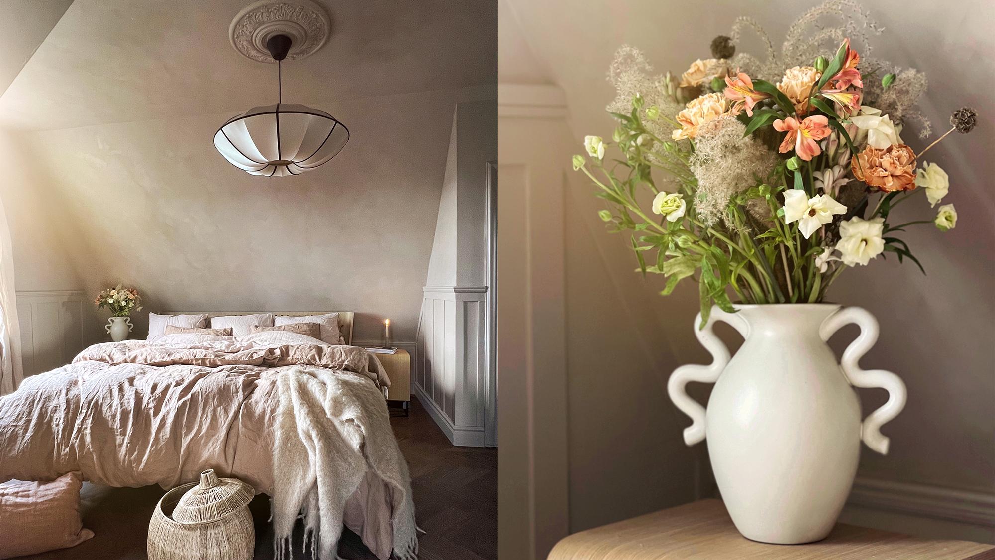 A cozy bedroom with neutral linens and a sculptural pendant light; next to it, a white vase with decorative handles holding a pastel flower bouquet.