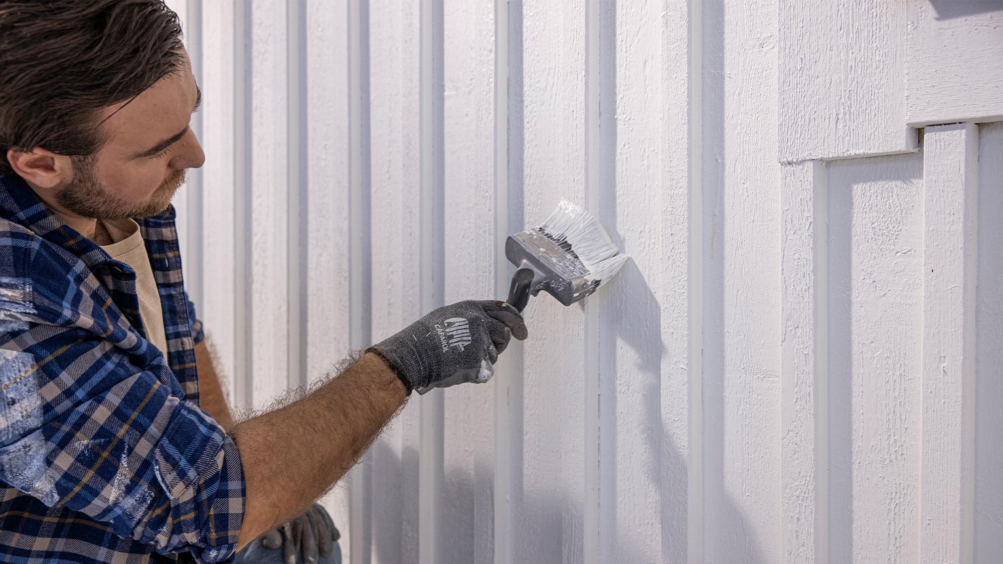 Man painting a white wooden wall with a brush.