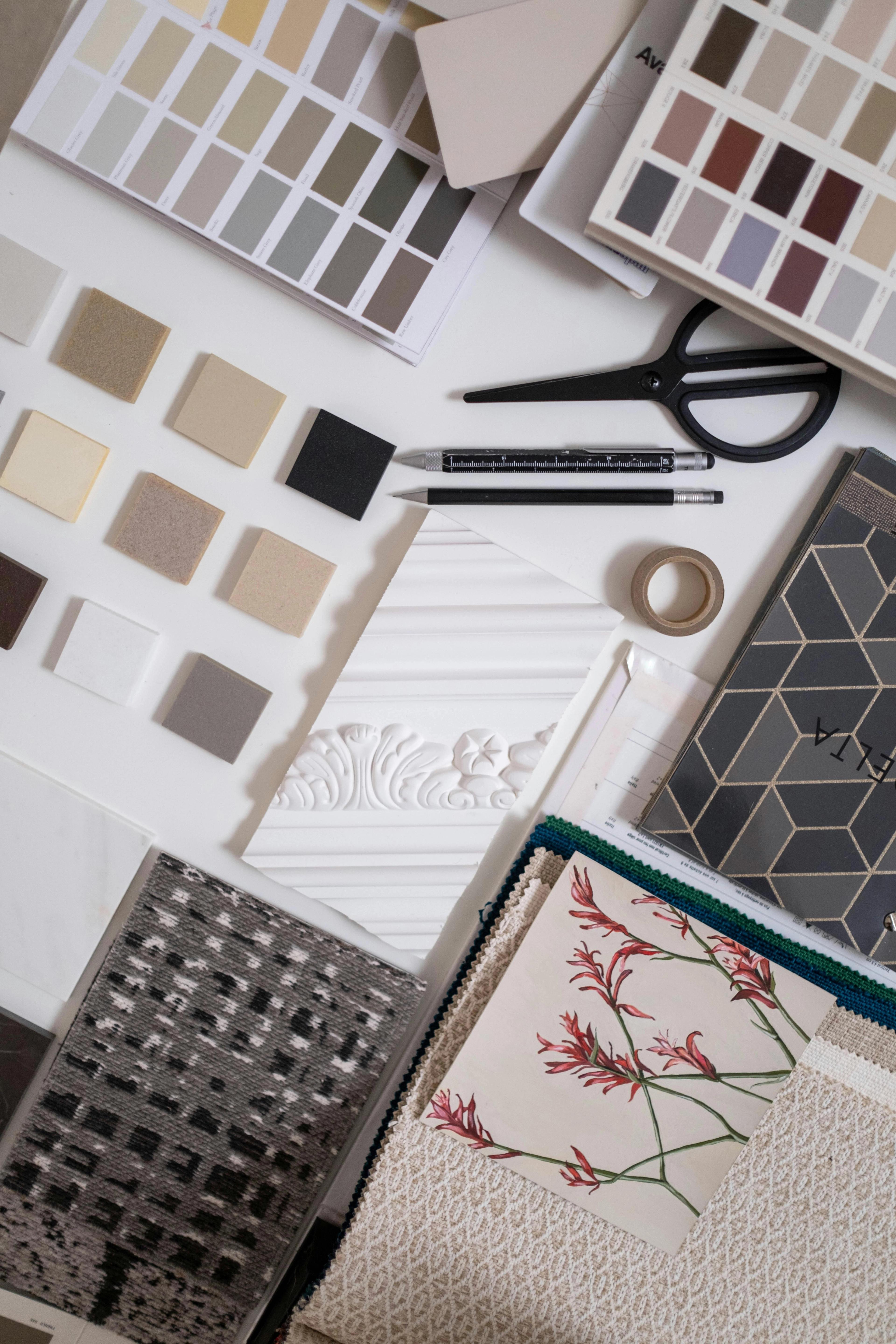 A flat lay of interior design samples including color swatches, material squares, fabric swatches, decorative trim, and design tools.