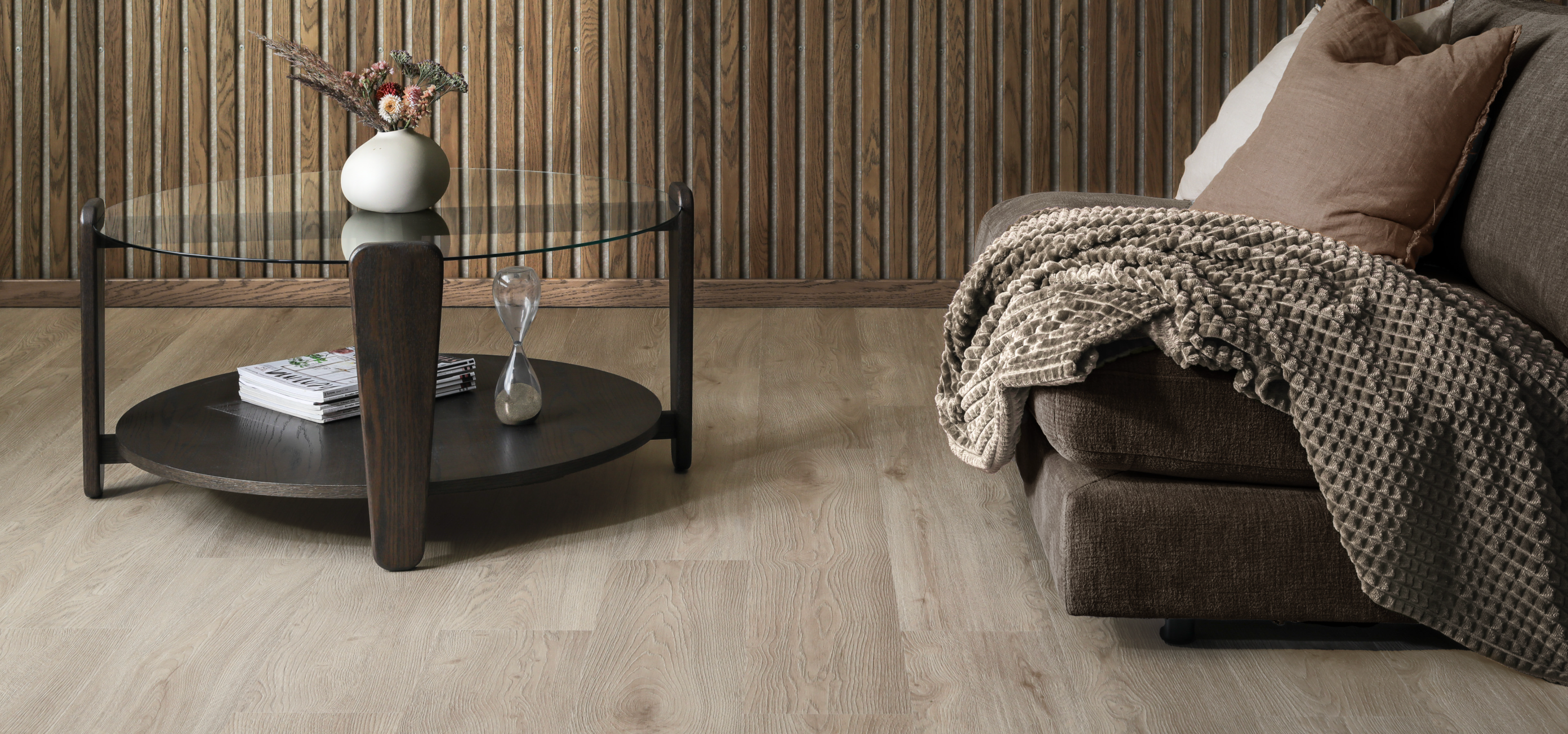 Living room with a dark wood coffee table, brown sofa, light wood floor, and slatted wood wall.
