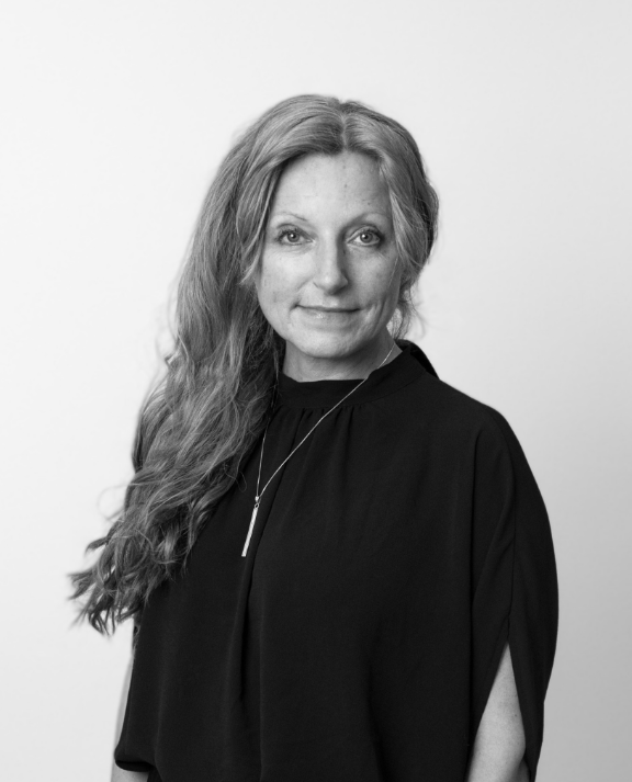 Black and white portrait of a smiling woman with long, wavy hair, wearing a dark top and a pendant necklace.
