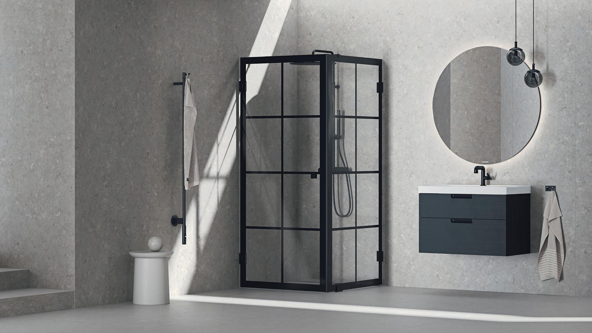 Modern gray bathroom with a black-framed glass shower, dark floating vanity, and a backlit round mirror, bathed in sunlight.