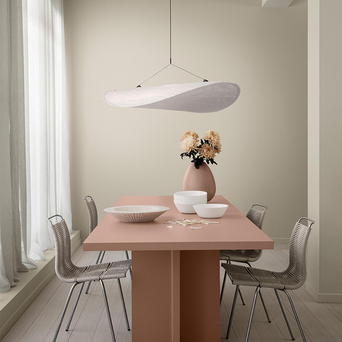 Dining room with a pink table, gray woven chairs, a wavy white pendant light, and pale green walls.
