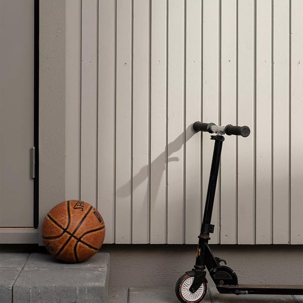 A basketball rests on a step beside a door, with a black scooter parked against a light wooden wall.