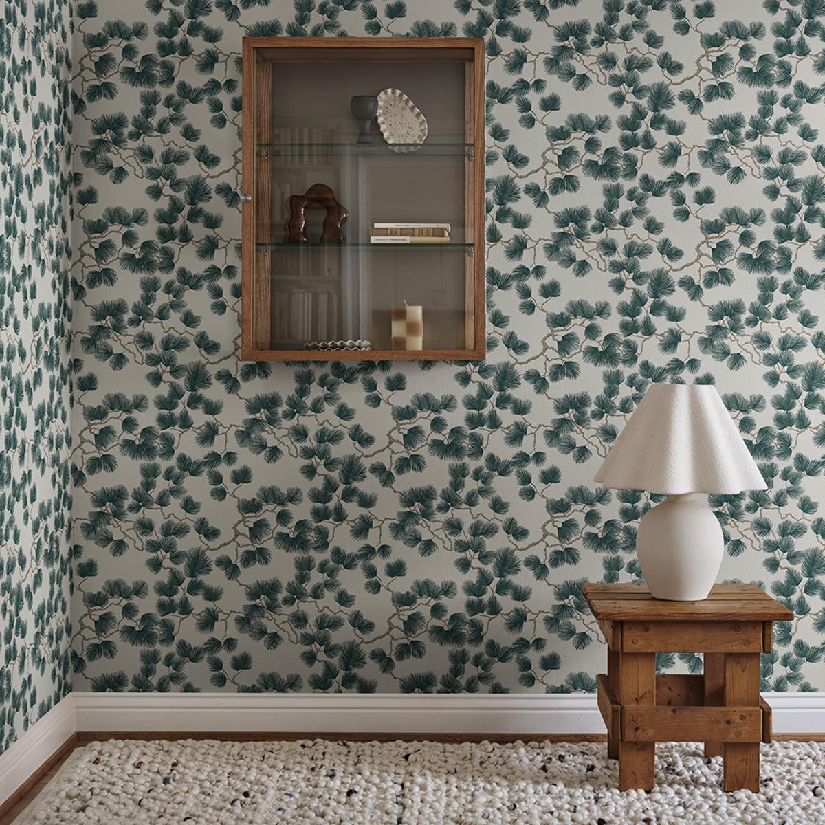 Walls with dark green leafy branch wallpaper, a wooden display cabinet, a white lamp on a wooden stool, and a textured white rug.