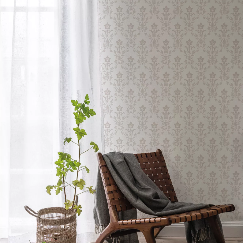 Interior scene with light patterned wallpaper, a potted plant, and a leather chair draped with a gray blanket.