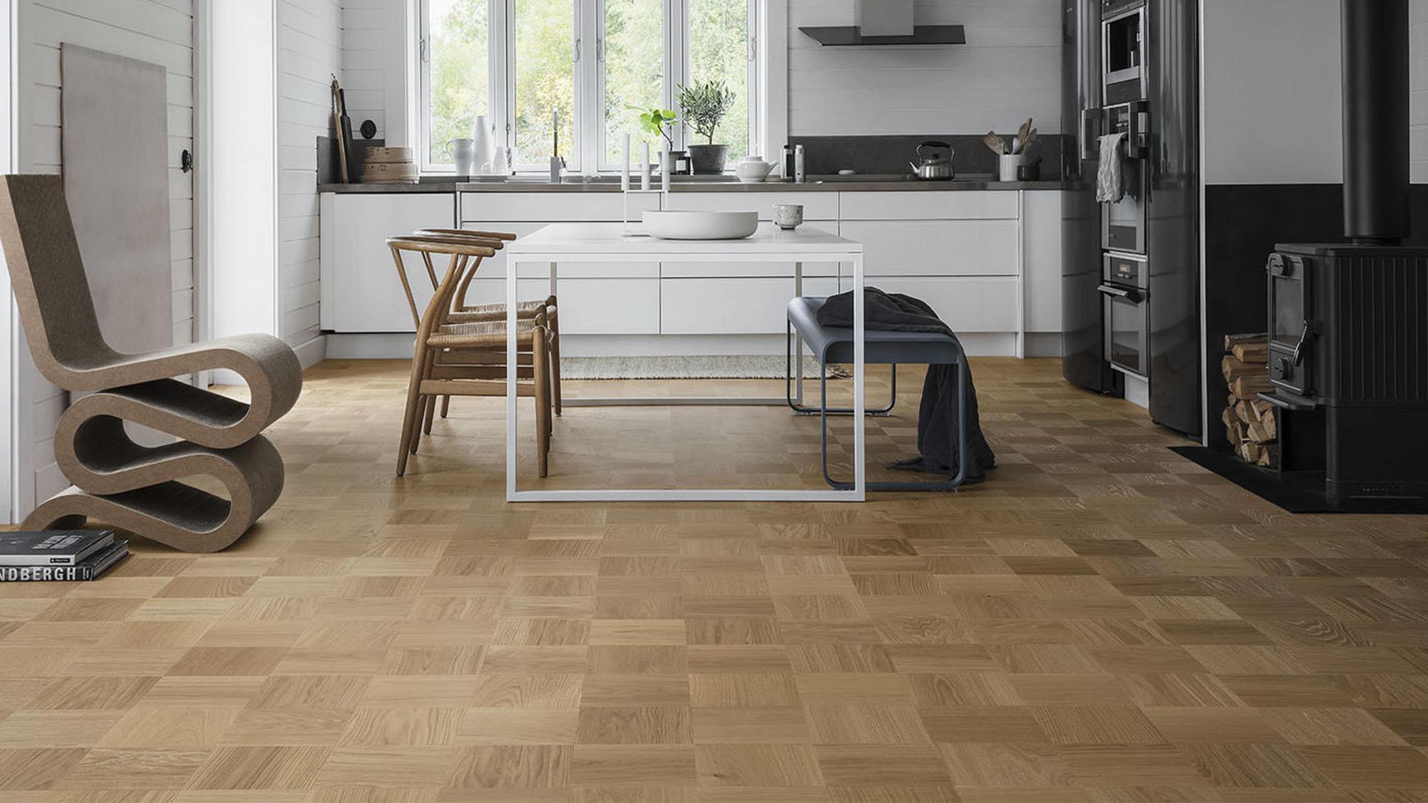 A modern kitchen and dining area with light wood square-patterned flooring, a wavy cardboard chair, and a wood-burning stove.