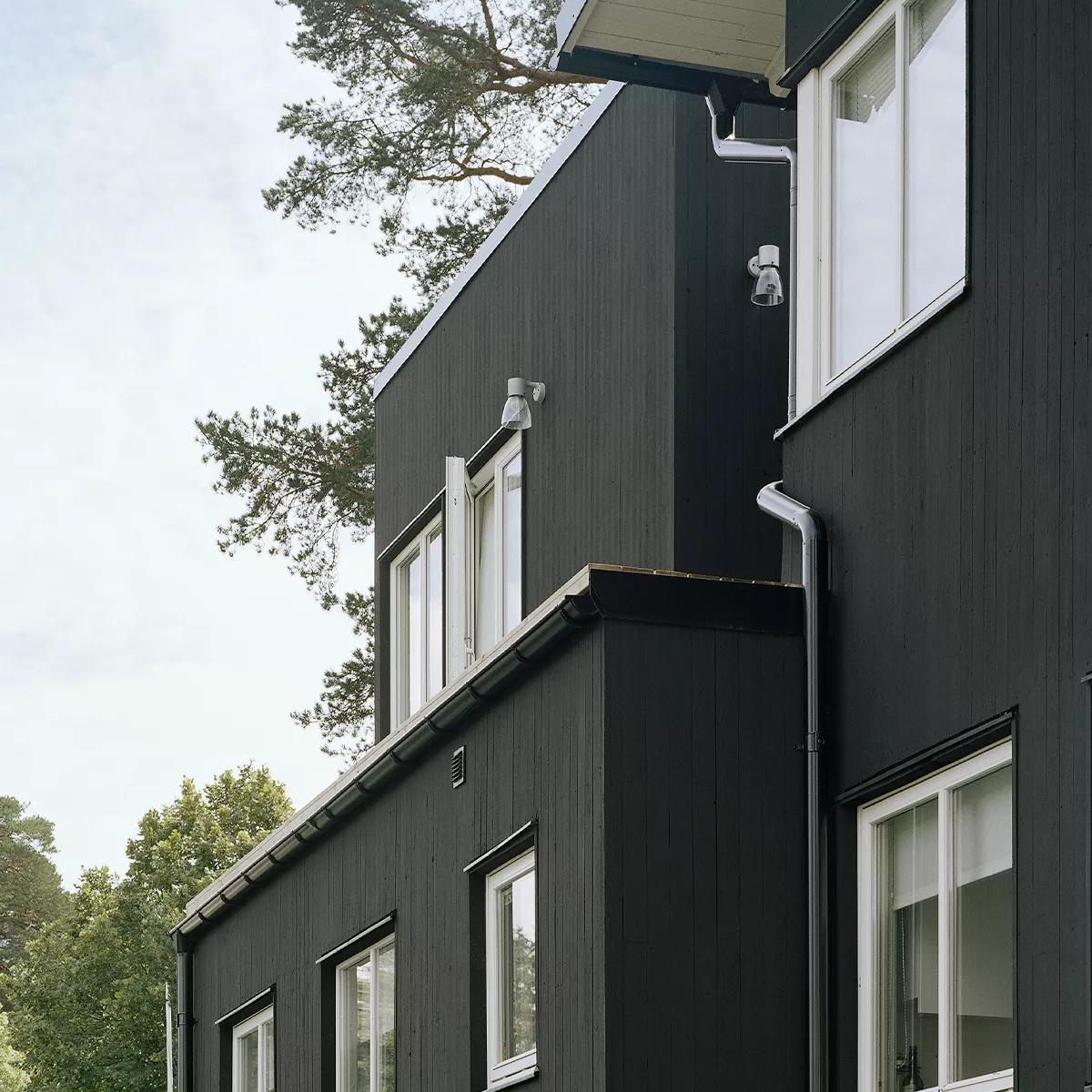 A modern building with black wood siding, white windows, silver gutters, and trees in the background.