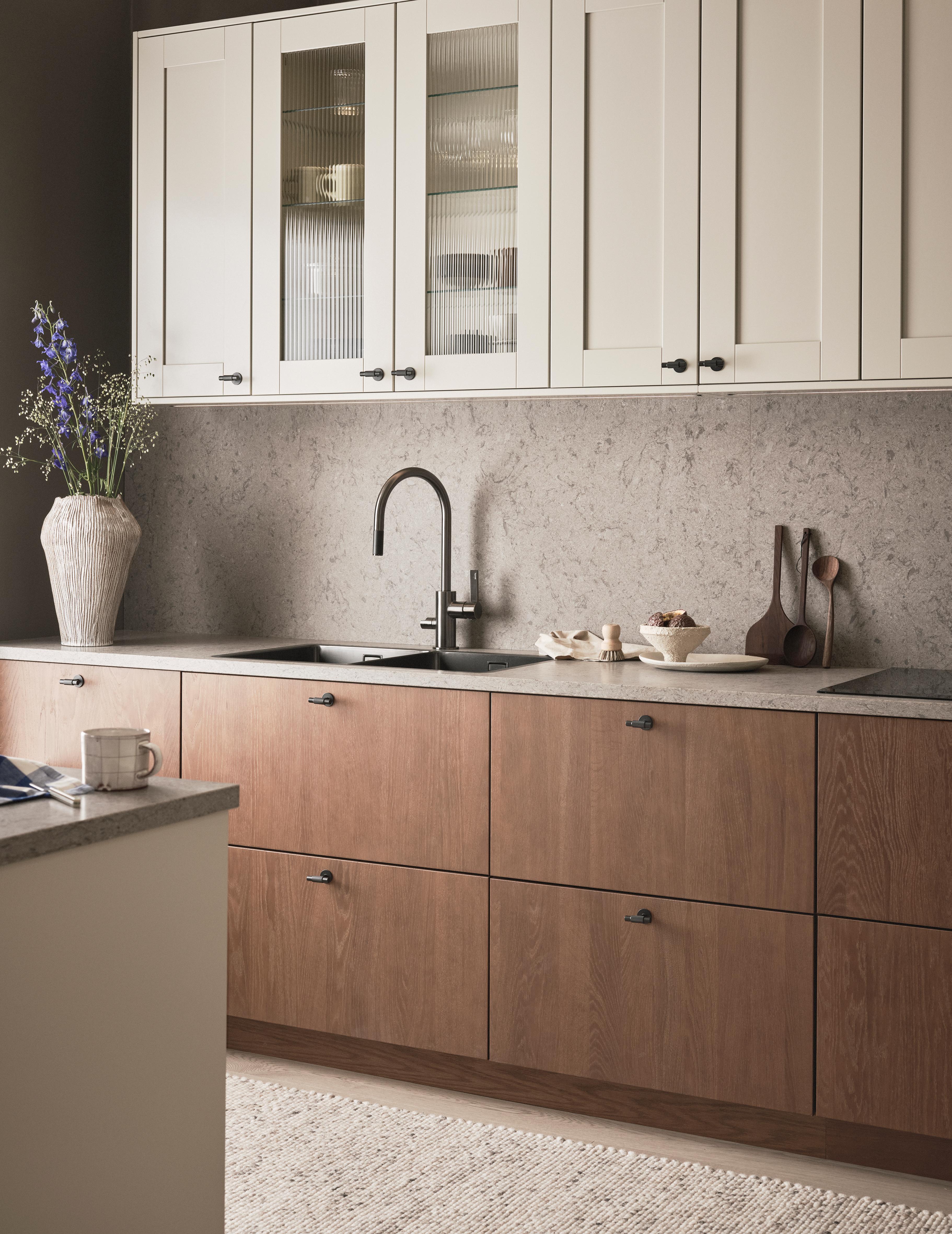 A modern kitchen with light upper cabinets, wood lower cabinets, stone countertops, and a dark faucet.