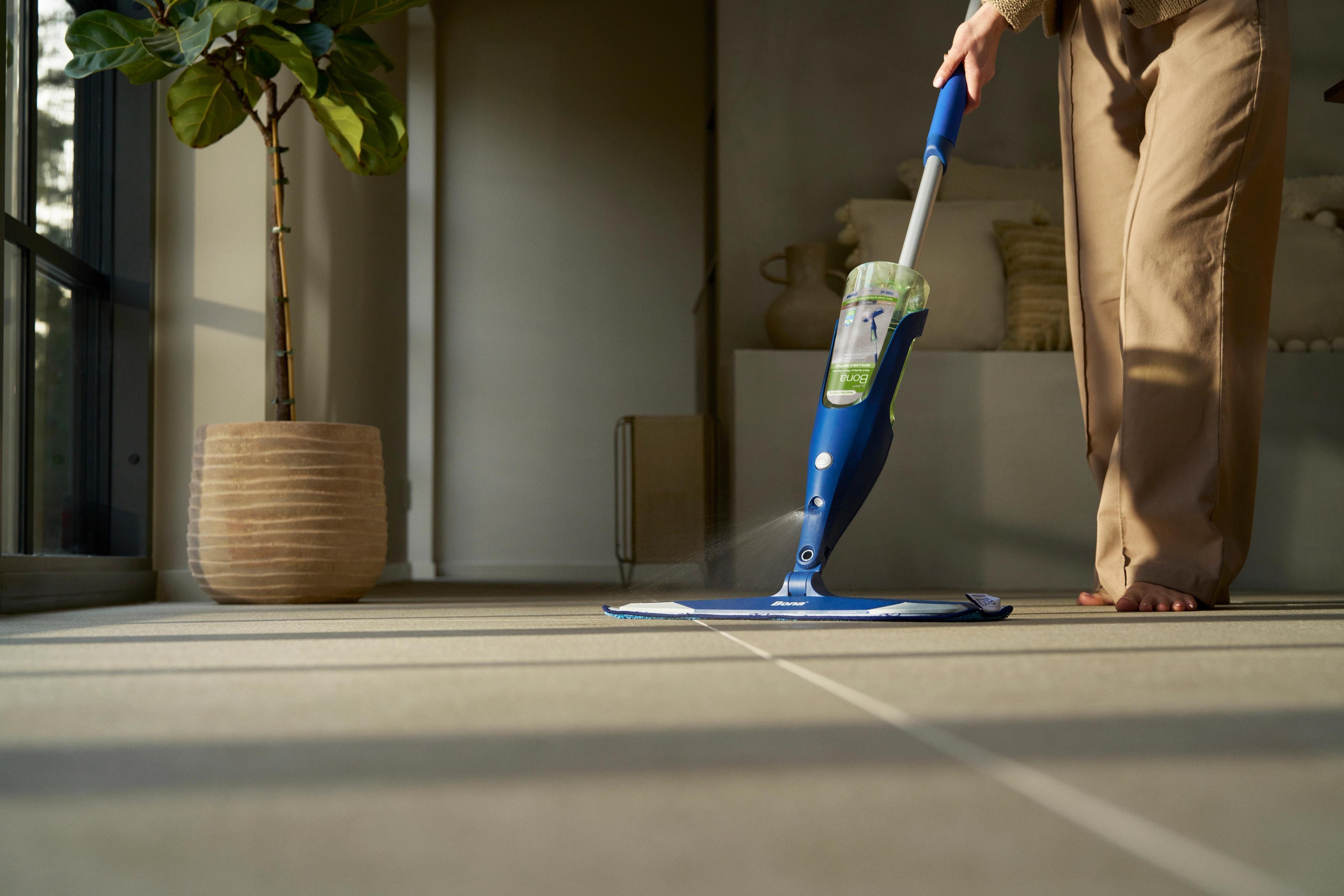 A person mops a tiled floor with a blue spray mop.