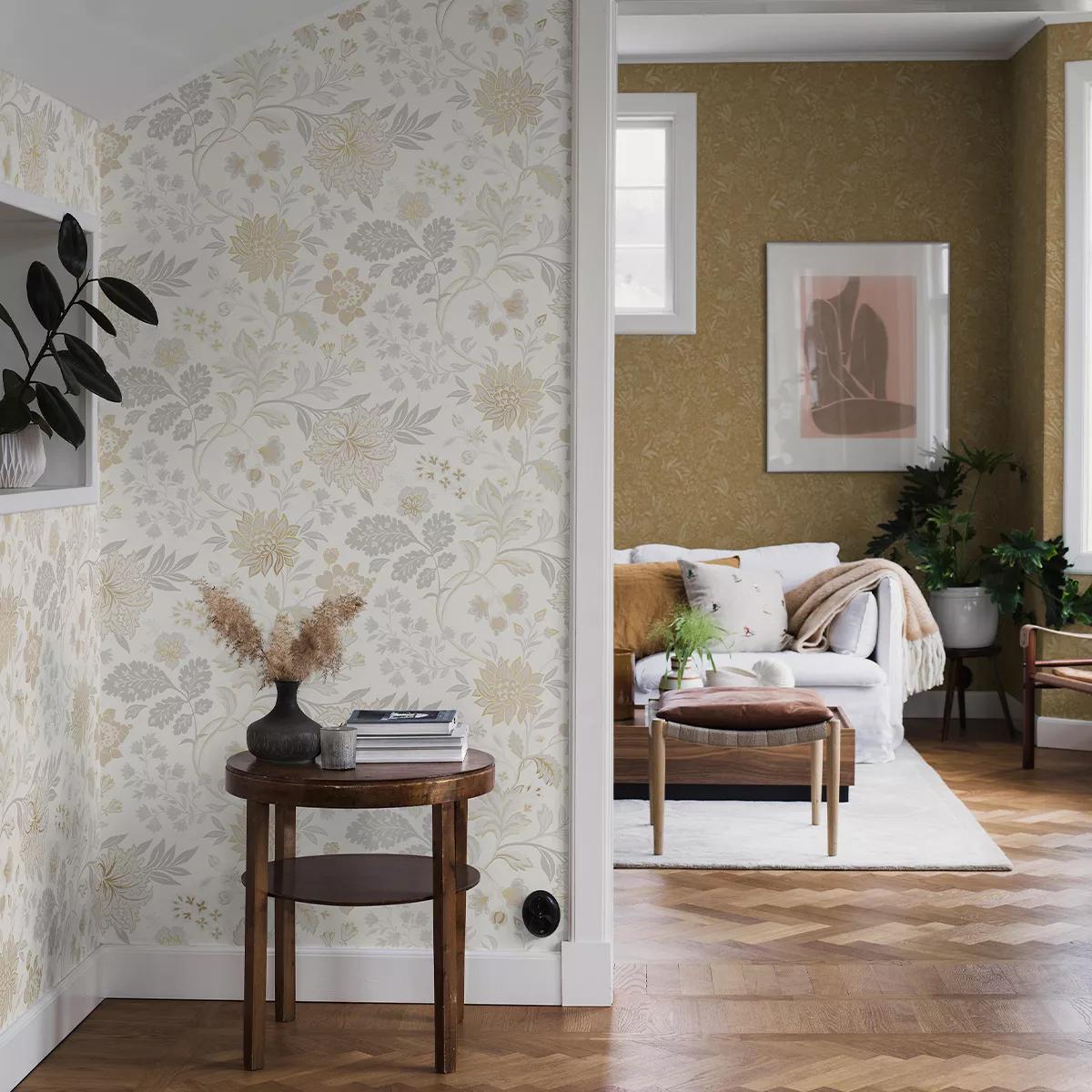 A hallway with light floral wallpaper and a small table leads to a living room with golden-yellow walls, a white sofa, and framed artwork.