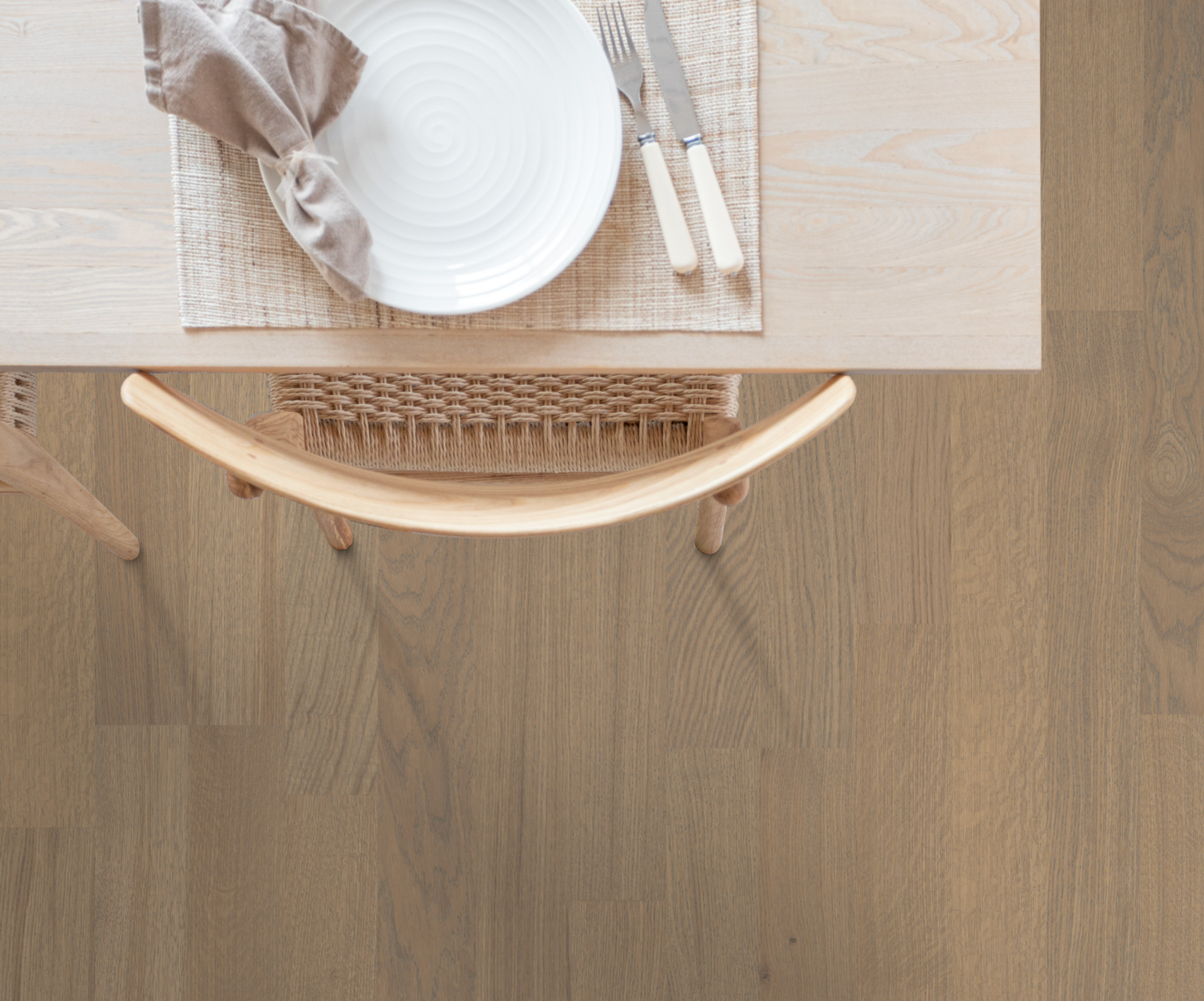 Overhead view of a dining table with a place setting and a wicker chair on light wood flooring.