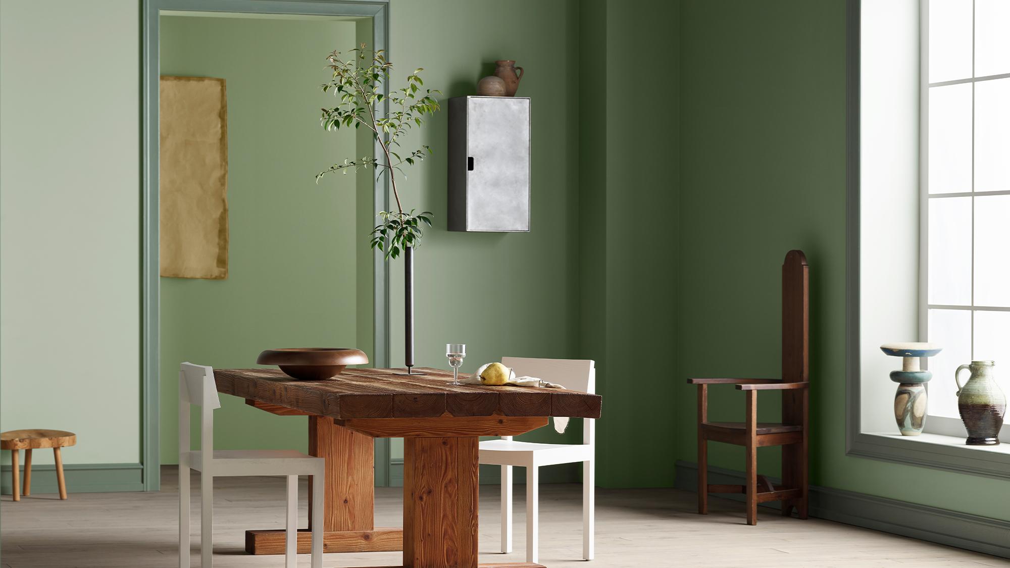 A dining room with two shades of green walls, a rustic wooden table, modern white chairs, and a tall wooden chair.