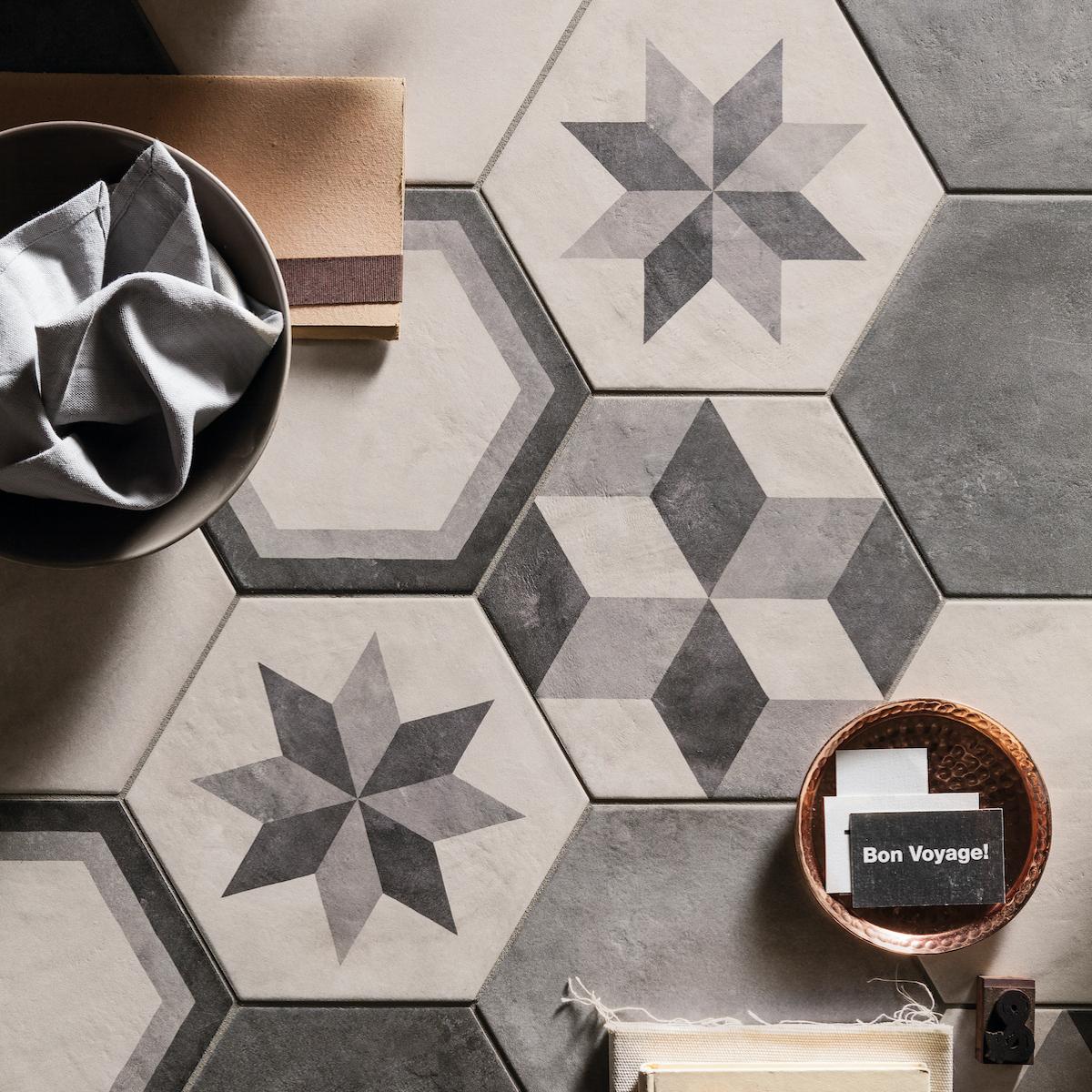 Hexagonal tiles in various grey tones, patterned with stars, 3D cubes, and outlines. A bowl, notebook, and small copper dish are on the surface.