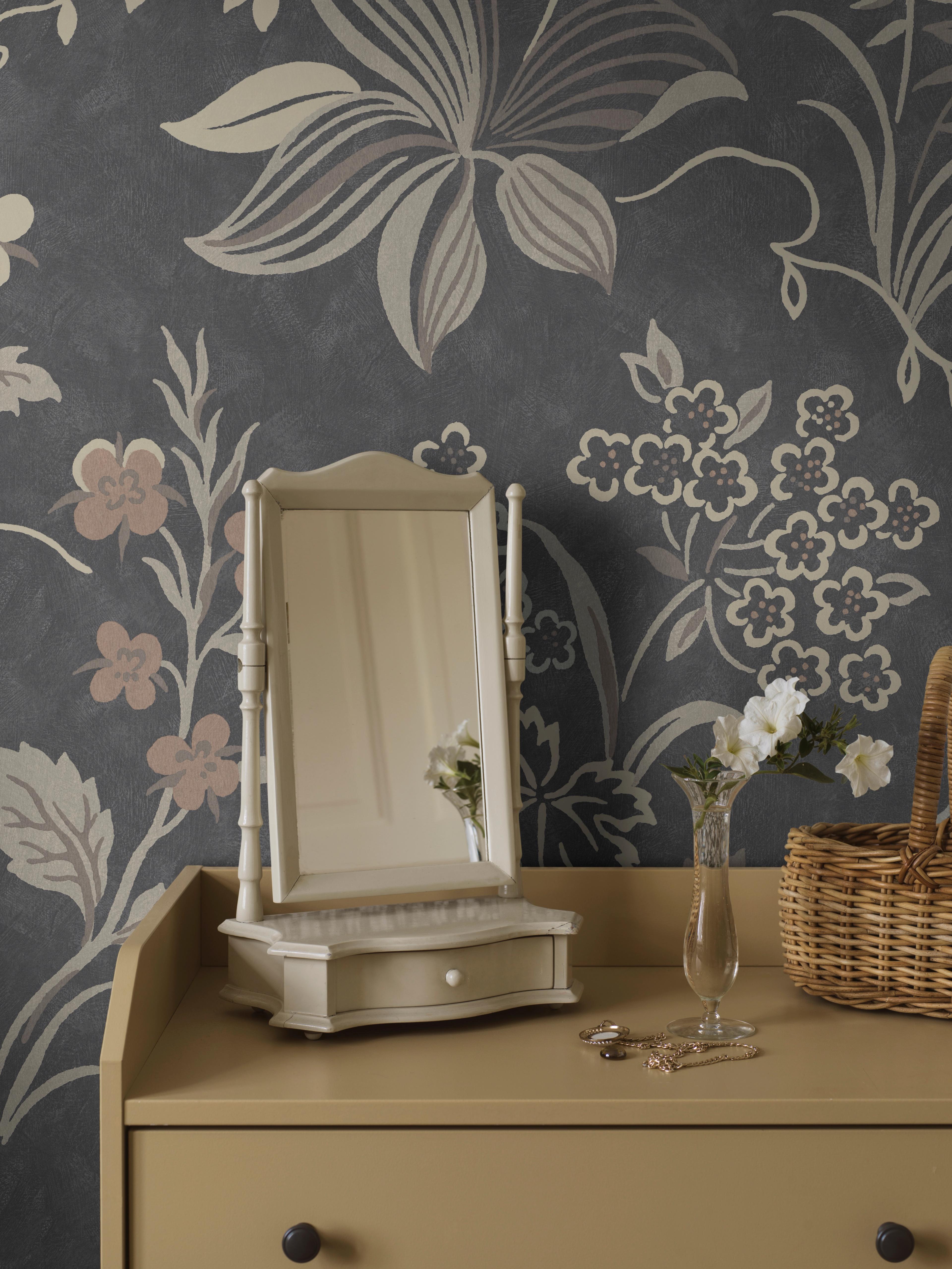 Cream vanity mirror on a beige dressing table against a dark gray floral wallpaper, with a vase of white flowers and jewelry.