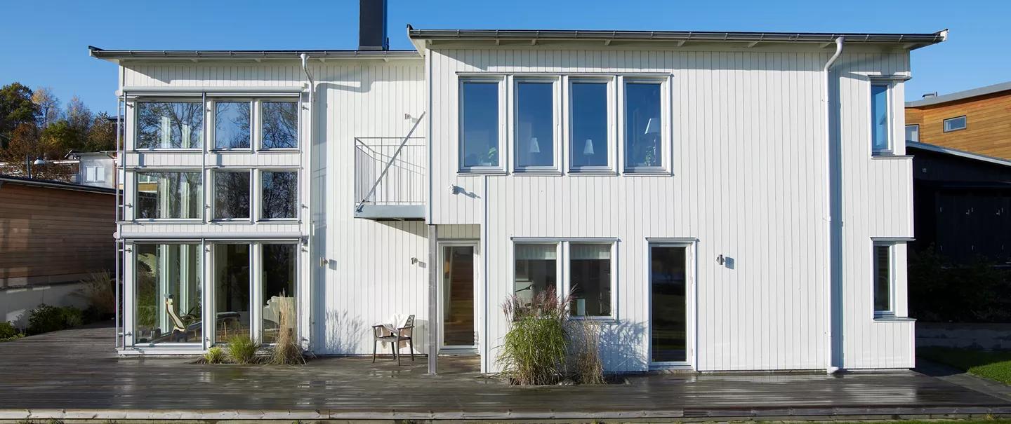 A modern white two-story house with large windows and a wooden deck.