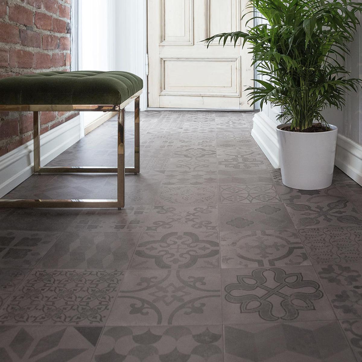 Grey patterned floor tiles in an entryway with a green velvet bench and a potted plant.