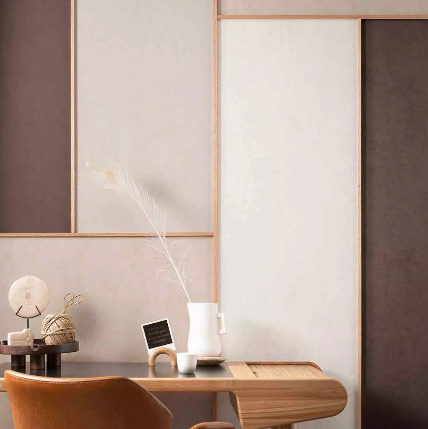 A minimalist desk setup with a feather in a white pitcher, various decorative objects, and a brown leather chair, against a paneled wall.