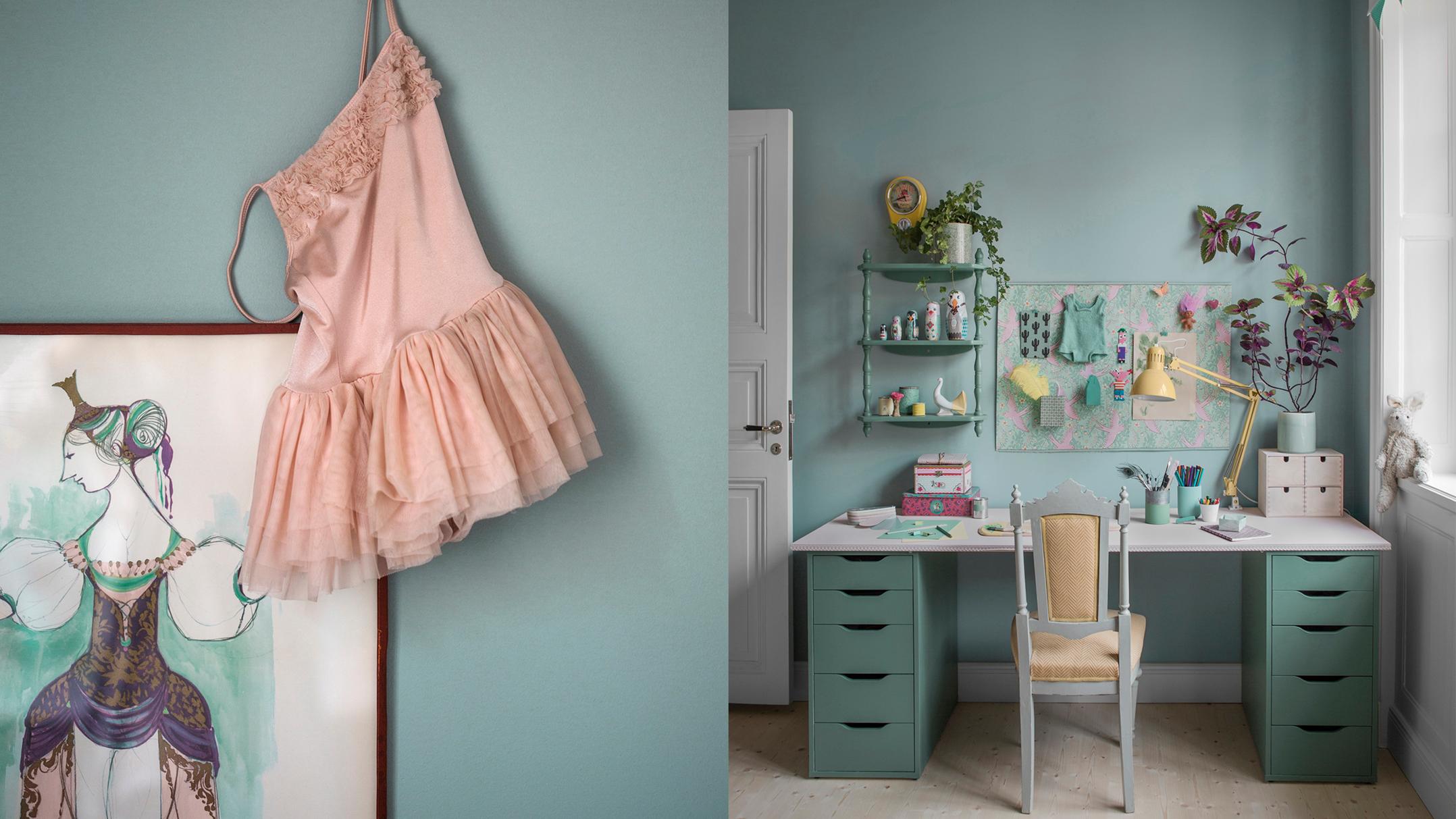 A pink ballet dress hangs over framed art on a blue wall, beside an organized craft desk with mint green drawers and a yellow chair.