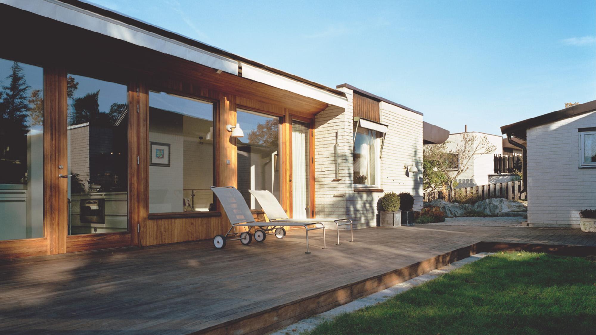 Exterior view of a modern house with a wooden deck, sun loungers, and a lawn.